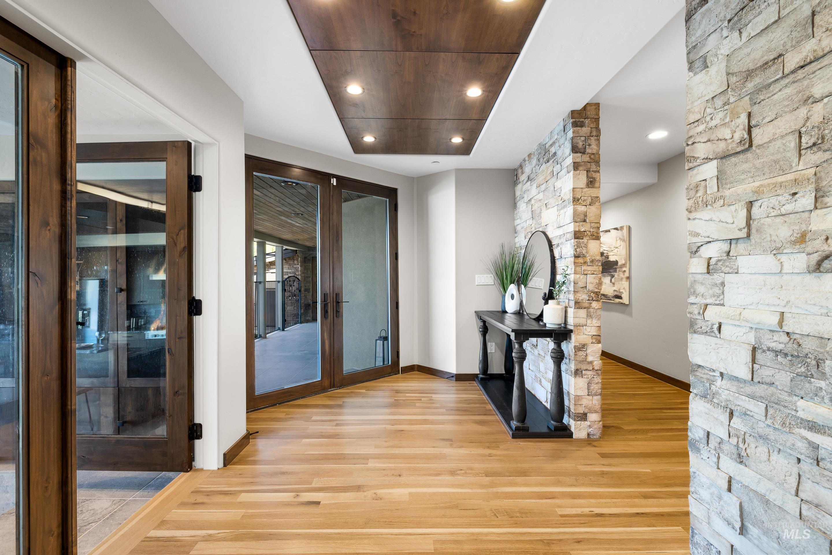 Foyer featuring wood-finish flooring, two sets of glass-paneled wooden doors, natural stone accent walls, and a recessed ceiling panel with integrated lighting