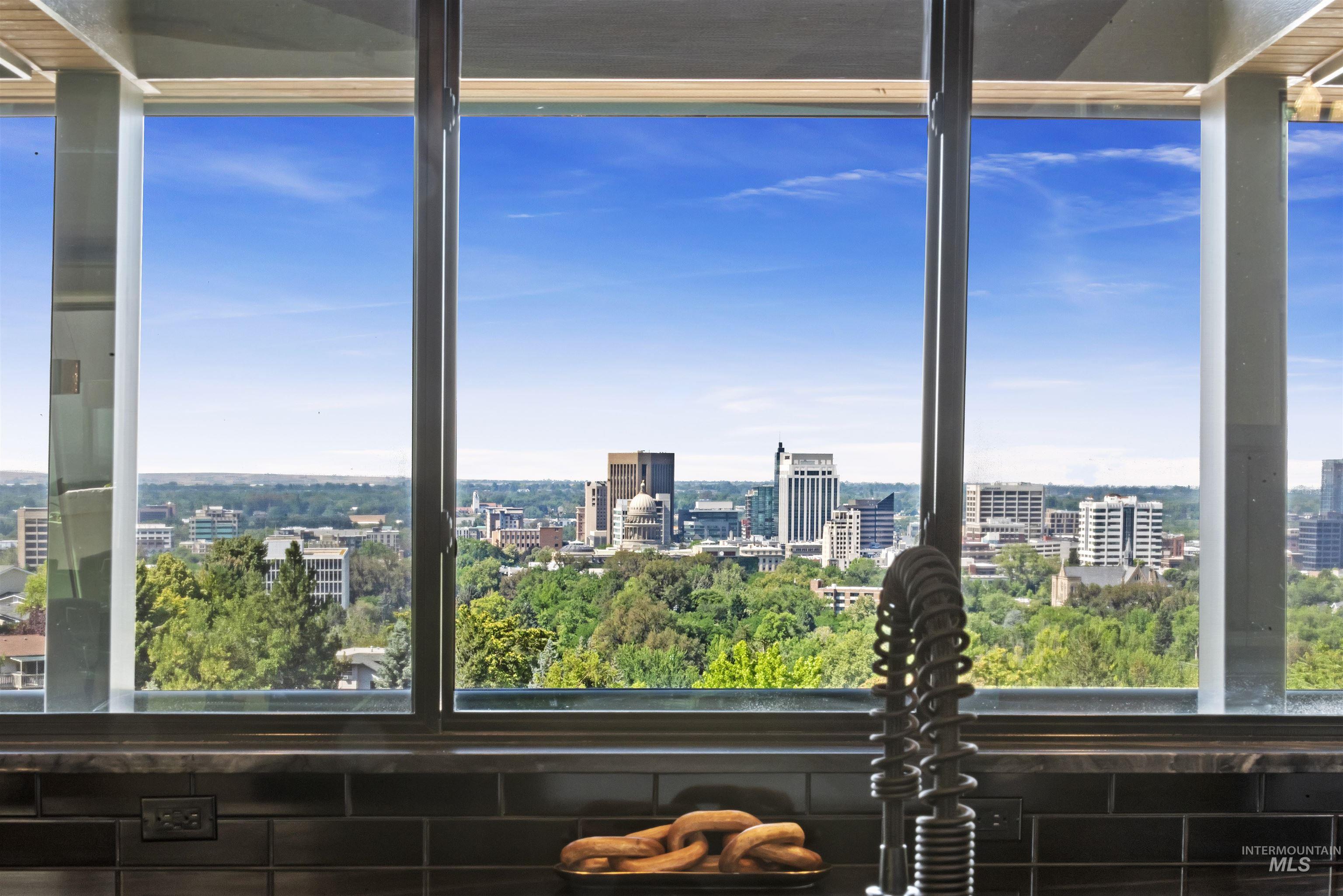 Expansive window framing city skyline and distant mountains, complemented by dark subway tile backsplash and a contemporary gooseneck faucet