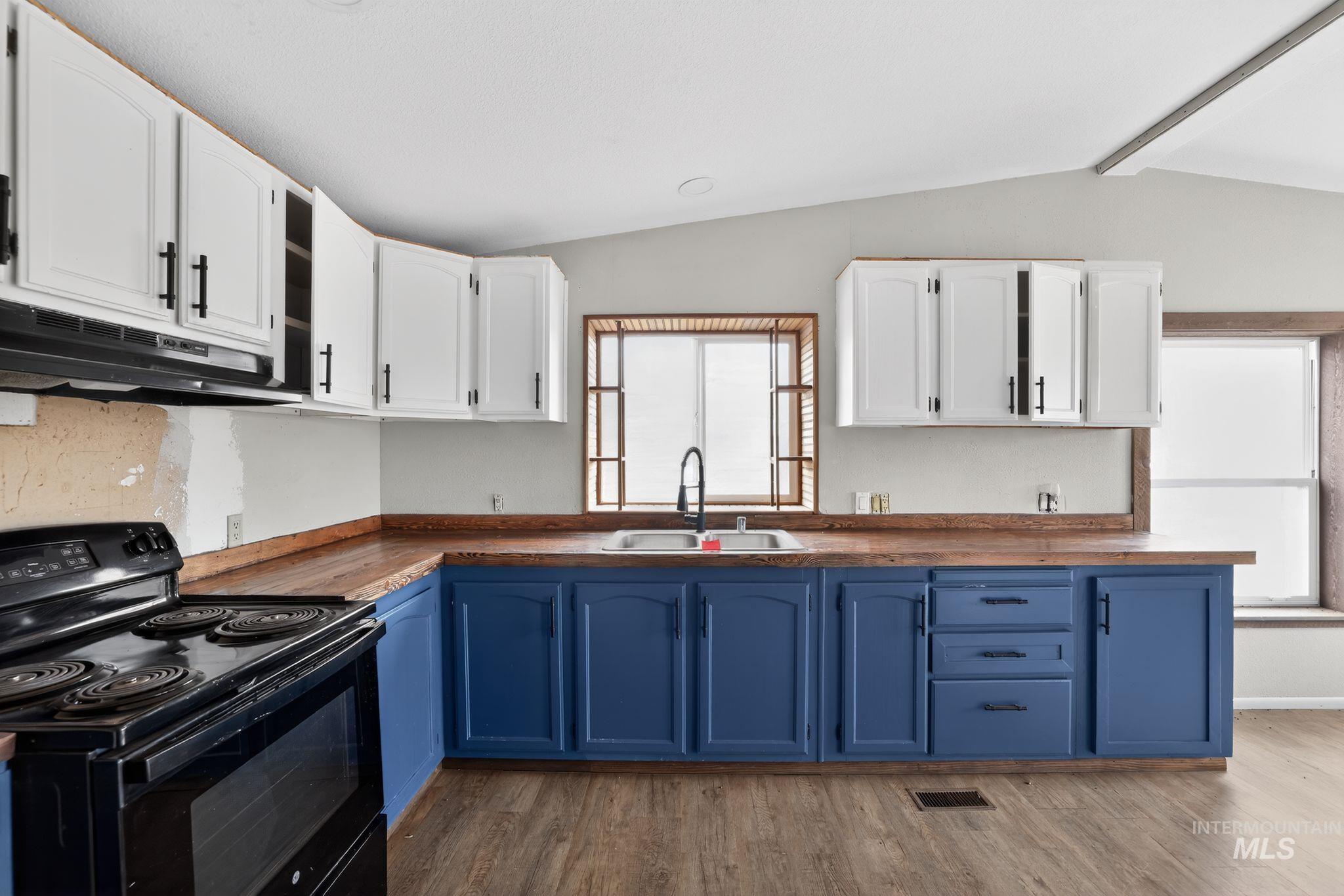 Kitchen with blue cabinetry, electric range, white cabinets, and lofted ceiling