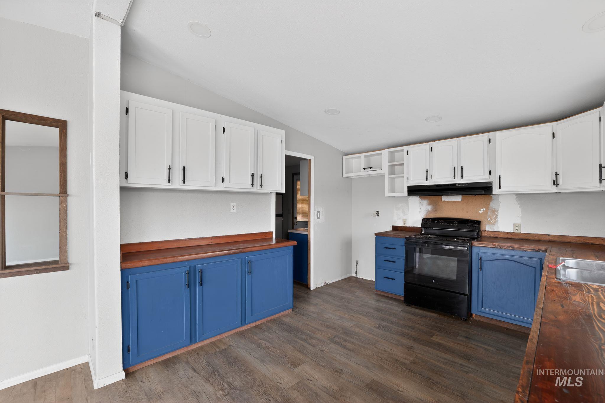 Kitchen with blue cabinets, black range with electric cooktop, white cabinets, vaulted ceiling, and butcher block counters