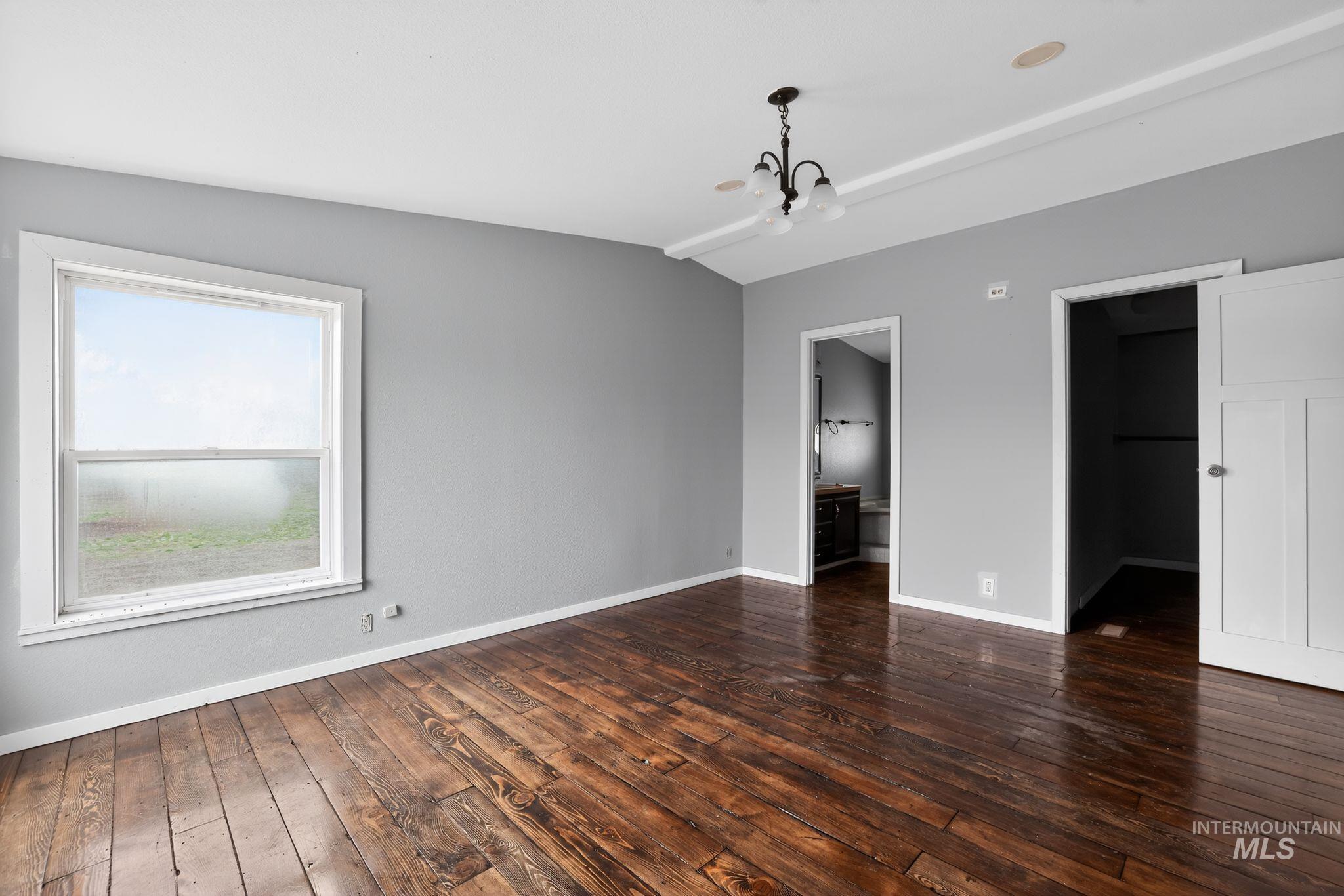 Unfurnished bedroom featuring dark wood-style floors, a spacious closet, lofted ceiling, a chandelier, and connected bathroom