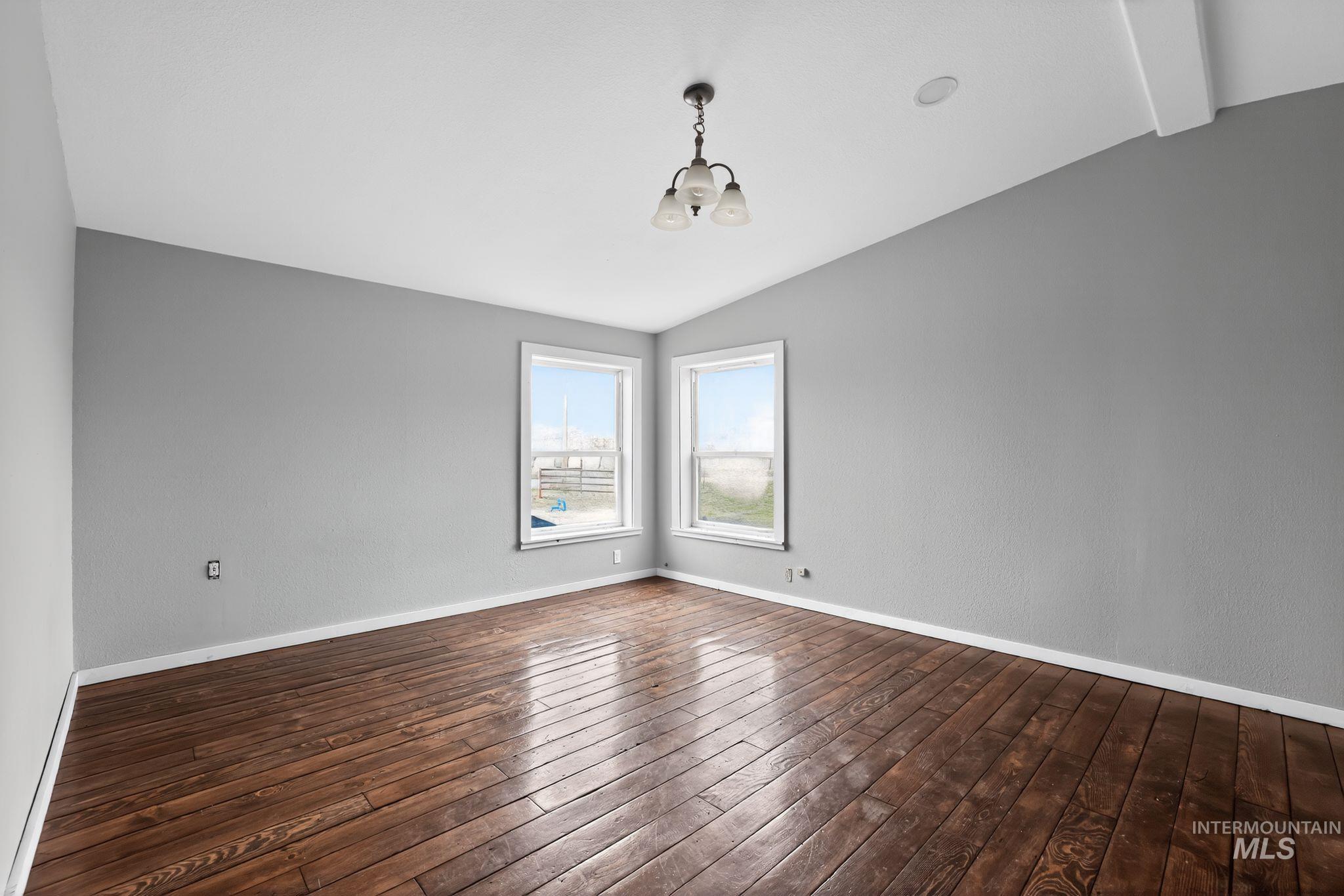 Empty room with lofted ceiling, a chandelier, and dark wood-style flooring
