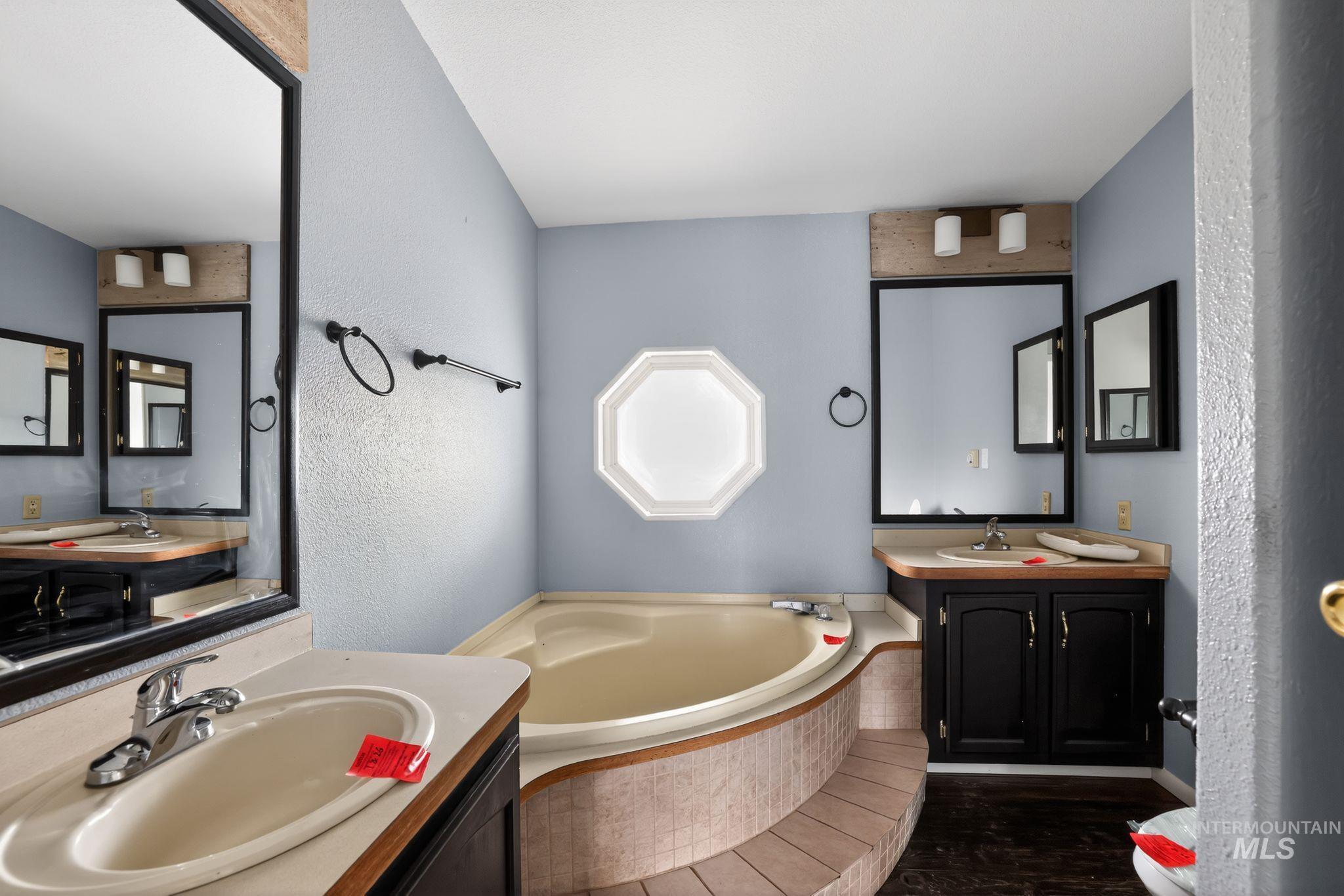 Full bathroom featuring two vanities, a textured wall, and a bath