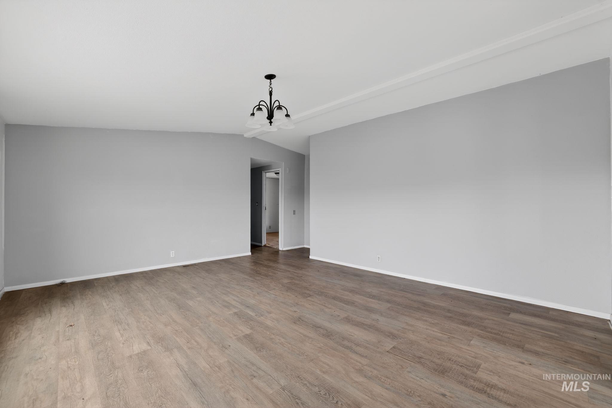 Spare room with a chandelier, wood finished floors, and vaulted ceiling
