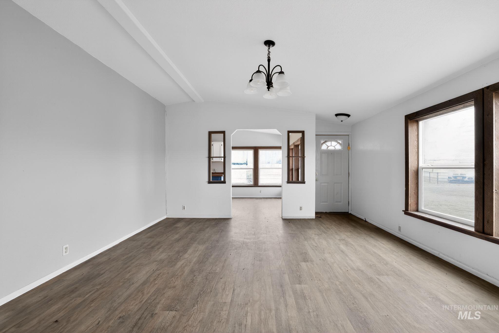 Unfurnished living room with a chandelier, wood finished floors, arched walkways, and vaulted ceiling