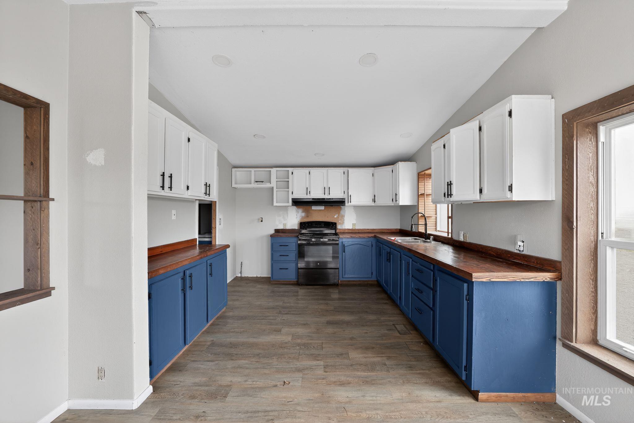 Kitchen with blue cabinets, butcher block countertops, white cabinets, black electric range, and lofted ceiling