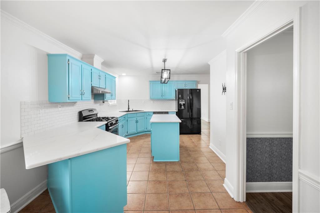 Kitchen with blue cabinets, stainless steel range with gas cooktop, pendant lighting, a kitchen island, and black refrigerator with ice dispenser