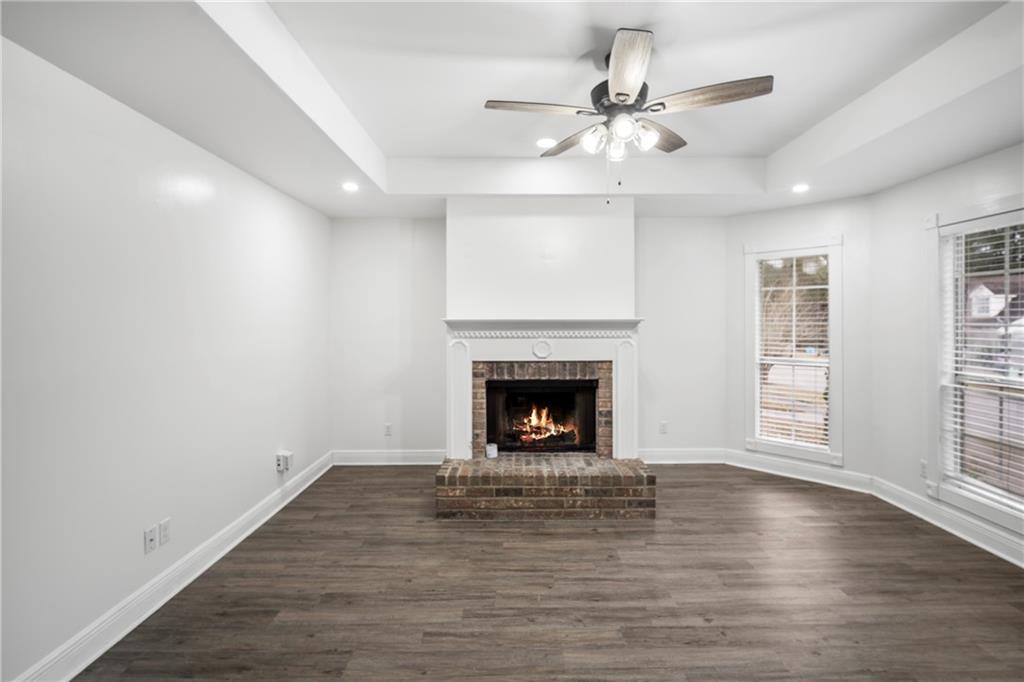 Unfurnished living room with recessed lighting, dark wood finished floors, a ceiling fan, a fireplace, and a tray ceiling