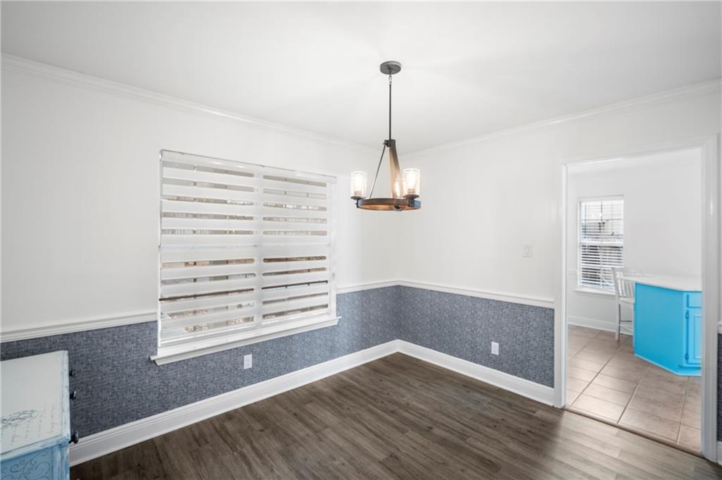 Unfurnished dining area featuring a wainscoted wall, a chandelier, crown molding, dark wood-style floors, and wallpapered walls