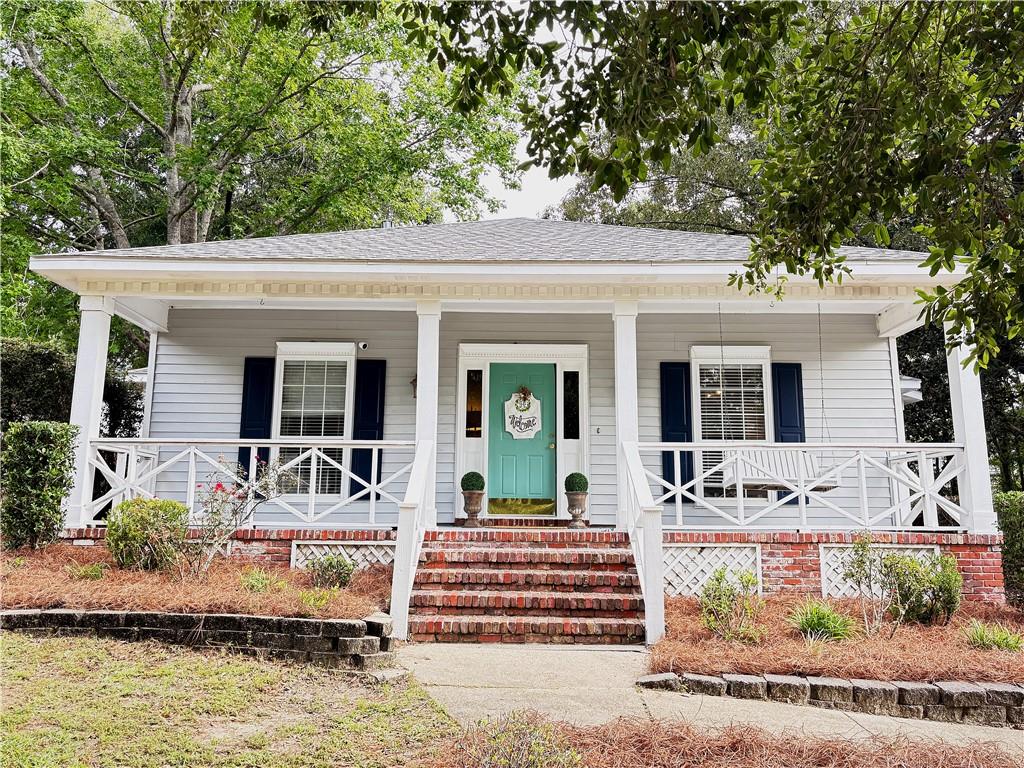 Light gray siding facade featuring a white columned front porch with decorative railing and a vibrant teal front door