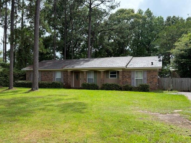 Brick facade ranch-style home featuring a covered front entry, mature front landscaping, and a shingled roof
