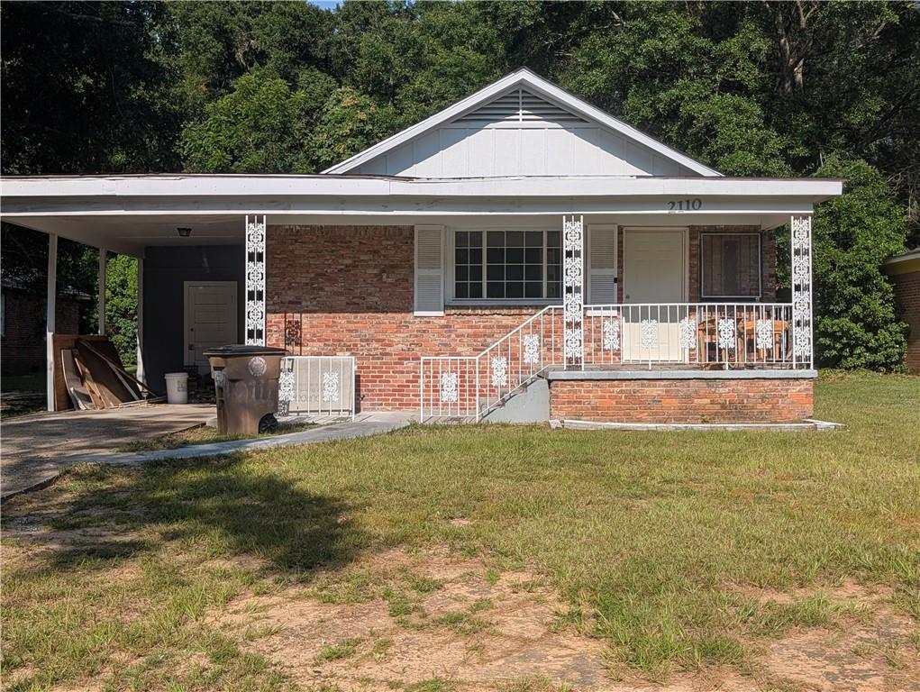 Brick facade residence featuring a covered front porch with decorative white railing, a carport, and a gabled roofline
