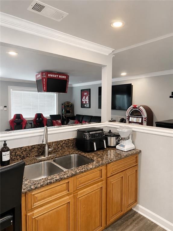 Wet bar featuring a double basin stainless steel sink, granite-style countertop, and wood-finish cabinetry