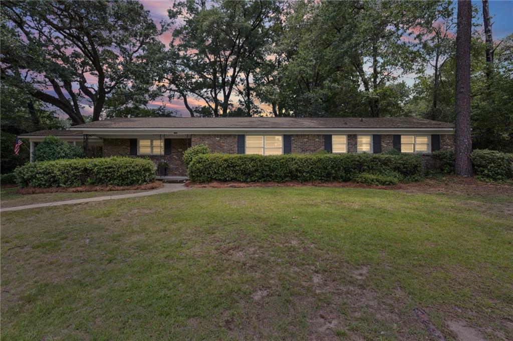 Brick exterior with dark shutters, established landscaping, and mature trees framing the property