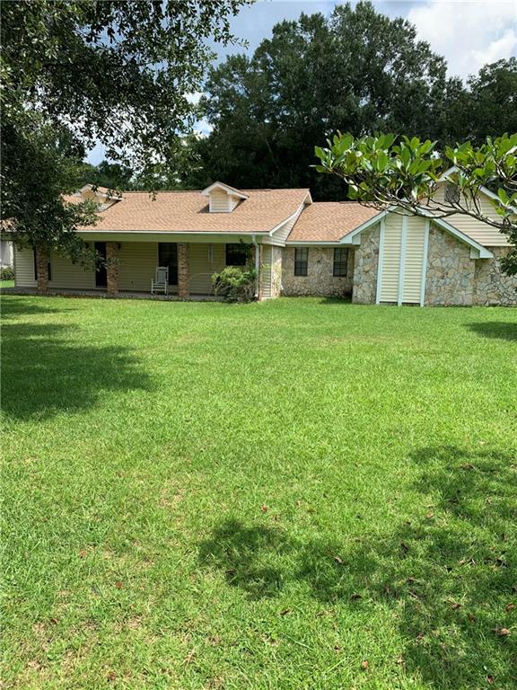 Rear view of house featuring a yard, stone siding, a shingled roof, and covered porch