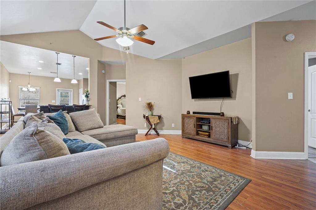 Living room featuring ceiling fan, light wood finished floors, lofted ceiling, and a chandelier