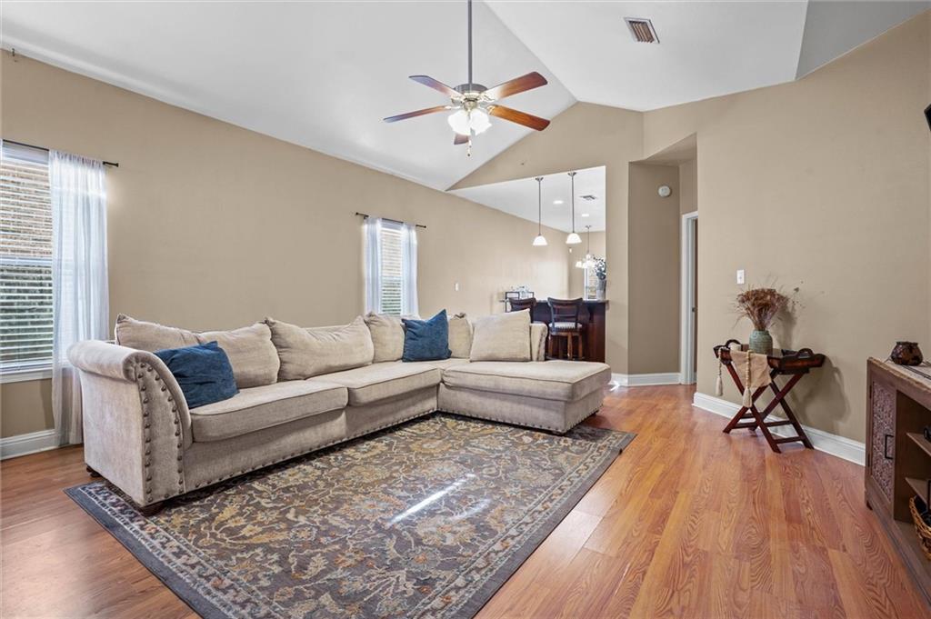 Living room featuring vaulted ceiling, light wood-type flooring, and a ceiling fan