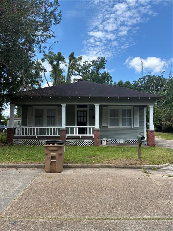 Front exterior featuring a covered porch, brick columns, and a dark entry door