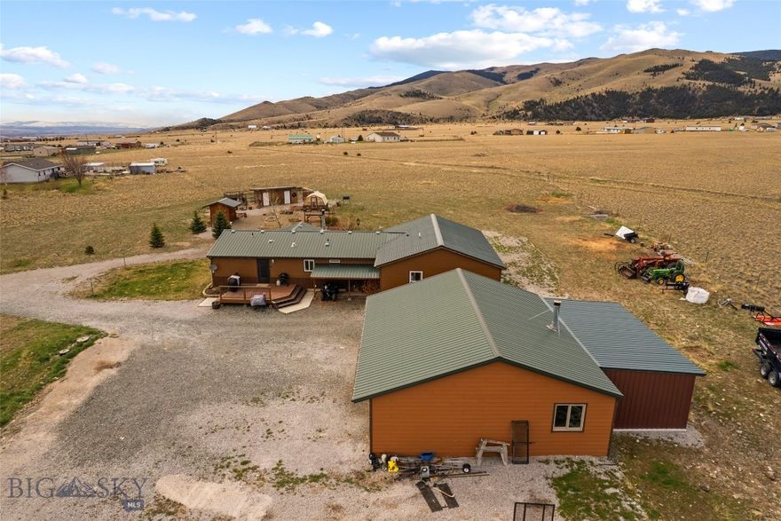 Wide open Montana living with room to breathe and views that go on forever. This well-kept single-level home sits on 3.61 acres surrounded by rolling hills and mountain backdrops, offering the kind of peace buyers are chasing. Inside, you’ll find an open-concept layout with warm wood finishes, abundant natural light, and a functional kitchen that looks out over the land. The living area is anchored by a cozy wood stove, creating that true Montana feel. Step outside and you’ve got space for animals, equipment, and projects—plus a large detached shop/garage and additional outbuildings already in place. Fenced yard, garden beds, and room to expand. A true homestead opportunity—quiet mornings, big skies, and the freedom to live how you want, all within reach of town.