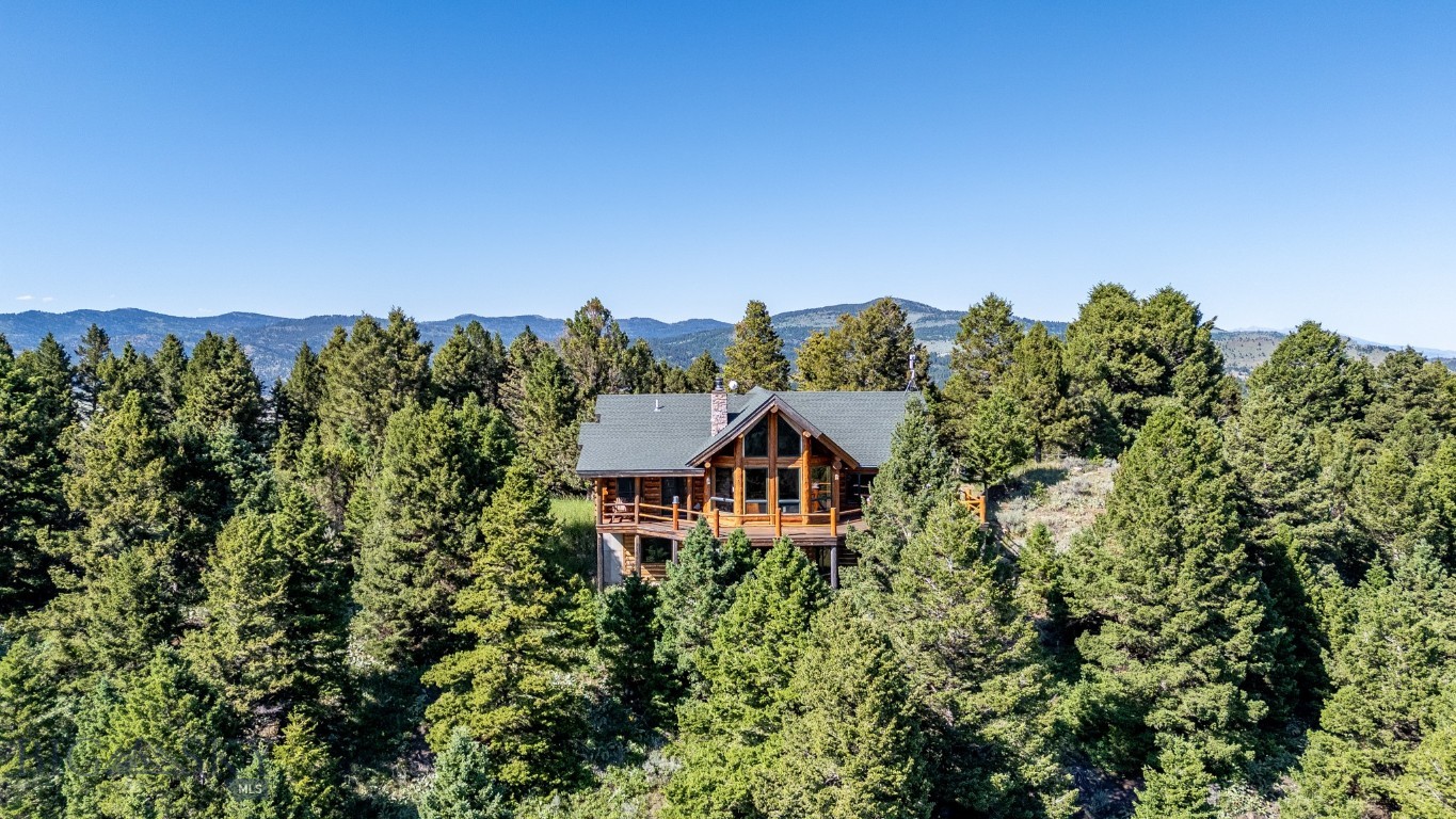 Escape to this beautiful log home on Johnny Martinez Trail, where rustic charm meets modern comfort in Bozeman's scenic foothills. Surrounded by towering pines and offering breathtaking mountain views in every direction, this property is pure Montana magic. The heart of the house is the dramatic great room with soaring timber ceilings, a stunning stone fireplace, and walls of windows that showcase those incredible views, while rich hardwood floors and warm log walls create a cozy yet sophisticated atmosphere throughout. The gourmet kitchen features beautiful wood cabinetry, granite counters, and stainless appliances – perfect for everything from morning coffee to dinner parties. The master bedroom is conveniently located on the main level, offering a peaceful retreat with log walls, forest views, and gorgeous vaulted ceilings, while upstairs you'll find a charming loft space accessible via a rustic staircase with natural wood railings that adds authentic mountain character. The basement level provides excellent additional living space with two bedrooms and a full bath, plus an unfinished area that offers endless possibilities for customization – whether you envision a home gym, media room, or whatever suits your lifestyle. The expansive deck is where this place really shines, with multiple outdoor spaces that take full advantage of the spectacular mountain views – perfect for morning coffee, evening drinks, or just soaking in Montana's natural beauty. Adding to the outdoor appeal is a private stocked pond on the property, perfect for casting a line right from your backyard or simply enjoying the peaceful water feature. Nestled on a private, wooded lot that feels like your own personal forest, you'll have complete privacy while still being convenient to Bozeman and Livingston, creating the perfect balance of mountain retreat and accessibility. This isn't just a house – it's your gateway to the Montana lifestyle, where every day feels like a vacation and every view takes your breath away.