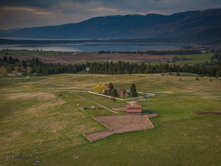 Mission Mountain Ranch is a 120-acre rolling foothill estate positioned at the end of a private road just minutes from the Flathead Lake resort community of Polson. Sweeping mountain, lake, and valley views frame a property that balances privacy and accessibility with a well-rounded set of residential and operational improvements. Sited on a subtle prominence, the +/-2,800 square foot home offers one bedroom and 1.5 bathrooms on the main level, with one additional bedroom, two bonus rooms, storage, and one bathroom below grade. The home is serviced by an oversized 2-car garage that doubles as a ranch shop, with adjacent covered parking for one additional vehicle. Two wells, septic, and power are all in place. Ranch infrastructure is solid and ready to work, with a 40x58 hay and horse barn, adjacent round pen, corrals, and automatic waterers. Covered equipment storage is on site, and additional cattle handling equipment and ranch machinery are available with the option to purchase. The entire property is enclosed with 5-wire fencing, and a fenced garden area with established fruit trees adds a welcome touch of self-sufficiency. The ranch is home to an array of wildlife including deer, elk and a variety raptors and song birds who meander on an off the adjacent public land.  Polson, a lakeside resort community of approximately 5000 is situated at the southern shore of Flathead Lake, set against the backdrop of the rugged Mission Mountains. The community offers a full range of amenities and services while retaining the character of a small Montana town. Both Missoula and Kalispell, full service communities, are just over 1 hour from the ranch.  For those seeking an intimate Montana retreat with the land, infrastructure, and setting to support both a working ranch and an exceptional quality of life, Mission Mountain Ranch is worth considering.