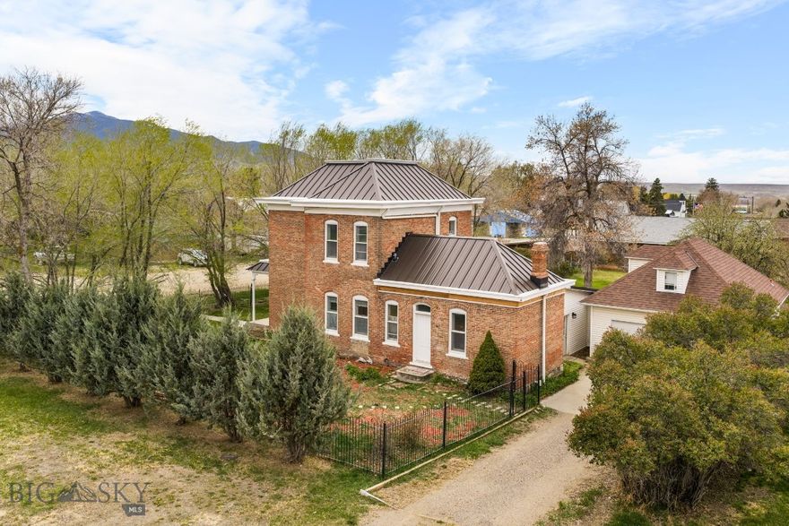 Less than 45 minutes to the renowned Madison River, the historic O’Brien House offers a rare blend of character, updates, and flexibility. This “small historic estate” is framed by a wrought iron fence, mature landscaping, and established grounds with fruit trees and a brick patio. Inside, you’ll find 12’ ceilings, original architectural details, and inviting living spaces, complemented by thoughtful updates including a remodeled kitchen with granite countertops and upgraded electrical (2020), new roof (2020), and new sewer line (2020). The home offers 2 bedrooms and 1.5 bathrooms, plus a sunroom with custom stonework and a flexible office/library space. A true standout is the attached additional living space, connected through the sunroom—ideal as a private third bedroom suite or as a separate 1-bedroom apartment with kitchenette and ¾ bath for income potential.
Additional features include underground sprinklers, drip systems, a powered homestead cabin relocated from Granite Creek—located near Virginia City, once the territorial capital of Montana and a central hub during the 1860s gold rush—and an equipment shed. A rare opportunity to own a historic property that lives well for both everyday comfort and long-term versatility.