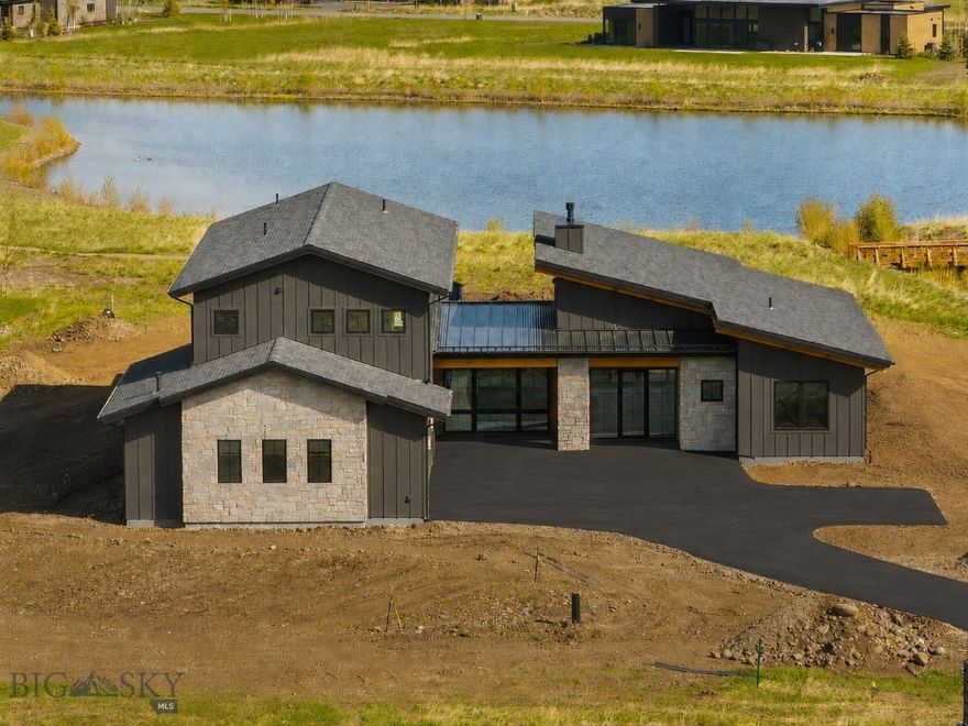 Set on 1.25 acres on the sought-after south side of Bozeman, this stunning new construction home in Home 40 blends elevated design, thoughtful functionality, and incredible views into one striking package. Backing to a peaceful pond with surrounding mountain views beyond, the setting feels both private and connected to everything that makes this community so special. Home 40 residents enjoy access to private ponds, miles of trails, a clubhouse, fitness center, and outdoor pool, all just minutes from Hyalite Canyon and downtown Bozeman. The home makes a strong first impression with beautiful stone accents, dramatic architecture, and a warm modern aesthetic. Inside, soaring ceilings and expansive windows flood the main living area with natural light, while a stunning fireplace with a stone hearth anchors the space. The kitchen was designed for both entertaining and everyday living, featuring Thermador appliances, quartz countertops, under-cabinet lighting, tile backsplash, a walk-in pantry, and seamless access to covered outdoor living spaces off both the dining area and kitchen. The main level offers a thoughtfully designed layout with a luxurious primary en-suite, spacious laundry room, powder bath, additional bedroom, and full bathroom and office. The office is entered through a custom glass wall, with floor-to-ceiling windows overlooking thoughtfully designed landscaping, creating a bright, architectural workspace with a calm, connected feel. The primary suite features dual walk-in closets, a freestanding soaking tub, dual-head walk-in shower, elevated finishes, and under-vanity ambient lighting. Just off the oversized three-car garage, the mudroom offers built-in storage, coat hooks, and space for organizing gear, while the heated garage offers ample storage. Upstairs, a generous flex space is surrounded by three additional bedrooms, all with walk-in closets. One bedroom includes an ensuite bath, while the other two share a Jack and Jill layout. Additional highlights include central air conditioning, seamless indoor-outdoor living, and a meticulously designed landscape plan featuring mature, statement trees that elevate the entire setting. Sophisticated yet inviting, bold yet timeless, this is the kind of home that turns heads while still feeling livable.