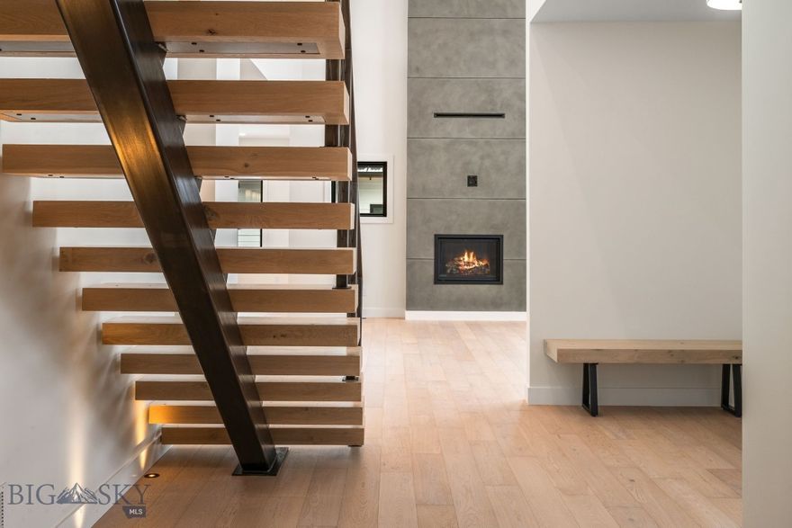 Experience elevated living in The Legends at Bridger Creek, one of Bozeman’s most coveted communities—where thoughtful architecture, exceptional craftsmanship, and extraordinary natural surroundings come together at the base of the Bridger Mountains. Defined by open space, trail connectivity, and true access to the outdoors, this premier neighborhood offers one of the most desirable settings in the Gallatin Valley. Directly across the street, Story Mill Park offers 60 acres of recreation with scenic walking paths, playgrounds, and seamless access to the East Gallatin River. The iconic Main Street to the Mountains trail system borders the subdivision, providing effortless connectivity to the College M and Drinking Horse hiking trails. Bridger Creek itself winds throughout the neighborhood, creating a peaceful environment. Bridger Creek Golf Course is just up the road, downtown Bozeman’s dining, shopping, and amenities are only minutes away, Yellowstone International Airport is easily accessible, and Bridger Bowl is less than 20 minutes from your door offering year-round recreation without sacrificing convenience. Inside, this stunning four-bedroom residence with a dedicated office and additional flex space delivers architectural impact from the moment you enter. A striking floating staircase framed by an expansive glass package sets the tone, filling the home with natural light and elegance. The heart of the home features an open-concept kitchen, dining, and living space designed for both everyday living and entertaining. Highlights include high-end appliances, custom cabinetry, tile backsplash, under-cabinet lighting, and a thoughtfully designed butler’s pantry providing storage and prep space. The living room is anchored by a dramatic floor-to-ceiling fireplace beneath soaring ceilings and oversized windows. Just off the garage, a functional mudroom with built-in seating and storage creates an ideal drop zone for Montana living, while a main-level laundry room adds everyday convenience. The main-level primary suite offers a private retreat with an expansive walk-in closet and a spa-inspired bathroom featuring an all-glass shower surround, dual vanities, a freestanding soaking tub, and luxurious heated flooring. Upstairs, you'll find three additional bedrooms, including one with its own private ensuite bathroom, an additional full bath, and a generous flex space offering versatility for guests, work, or extra living area.