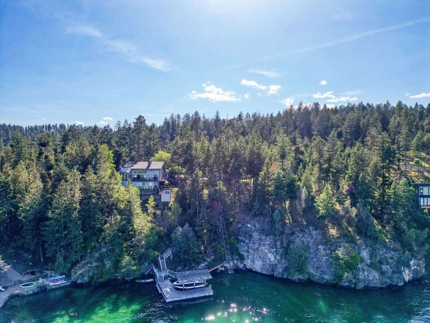 Perched above the sparkling waters of Flathead Lake, this extraordinary luxury estate offers sweeping views of the Swan Mountains & into Glacier National Park. Set on 2.67 private acres, on two lots with 251 ft. of pristine lake frontage, this property blends elegance, functionality, and Montana’s natural beauty. Every detail of this home has been thoughtfully enhanced with premium upgrades. A custom-designed funicular provides seamless access for all ages down to the water’s edge, where a beautifully upgraded dock system awaits, complete with a new hydraulic boat lift & a cantilever double PWC lift with interior catwalk. You will also find a mermaid pond at the water's edge. A charming nature pathway winds through the property, offering a scenic walk to the water. Outdoor living is unmatched with multiple sitting areas designed to take in the views, a cozy firepit for evening gatherings, and expansive decks-completely replaced and upgraded with glass railings to preserve the view. This home offers nearly 4,000 square feet of refined living space, including 5 bedrooms and 6 bathrooms, blending comfort and elegance with room for family and friends. The great room centers around a dramatic floor-to-ceiling river rock fireplace, with soaring vaulted ceilings that create a sense of grandeur and openness. The sunroom is a fan favorite among guests that have enjoyed it over the years, capturing year-round light and lake vistas. Wildlife carvings, including bears etched into the floor tiles, lend a bespoke, artistic touch that celebrates Montana’s wilderness spirit. Recent investments include a new HVAC system, boiler, furnace, paint, window treatments, two 24kW backup generators, and starlink high speed internet. A spacious attached triple garage provides convenience, while the separate heated shop offers ample space to store your boat, recreational gear, and seasonal toys. Fully equipped with a half bathroom, utility sink, and its own washer and dryer, the shop is designed with both functionality and comfort in mind—ideal for lake days, projects, or extended stays. Whether you're savoring the tranquil mountain vistas from the upper terrace, heading out for a day on the water, or simply unwinding in the serenity of your surroundings, this extraordinary Flathead Lake estate offers an unmatched retreat in the heart of Big Sky Country. This property is accessible year round.