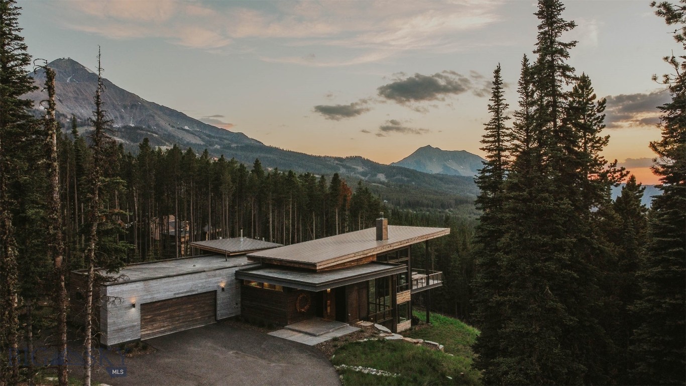 As you approach this mountain modern family home, designed by renowned Bozeman architect, Reid Smith, you will feel the unique privacy afforded by this spacious 2.1-ac forested lot. The house is built to the highest standards by long-time established, Big Sky Build, and is positioned to maximize the down-valley views looking west. Enter the home through the custom-designed, 9' door made from a live-edged, slab of center-cut walnut, and you will be struck by the unique proportions and flow of the home. Ideal for entertaining family and friends, the upper floor common area flows from the true chef's kitchen to the intimate dining area to a glass-encased living room. The award-winning Gyrofocus fireplace is a focal point of the living room, suspended from the cedar-lined ceiling as it rises to 17'. The impressive views will have you mesmerized by the sunsets from the outdoor living/dining/grilling area with a gas fire bowl. The sleek & functional kitchen is centered around a large island, encased in honed Brazilian marble that waterfalls at either end with a large Subzero fridge, 2 Wolf wall ovens, and a Wolf cooktop range. Custom-designed walnut cabinetry provides extensive storage & a pantry area with a coffee station. The wide staircase flows down to the lower family room with generous space to relax, watch movies, or exercise, the bunk room, an additional bedroom, and the spacious second master suite. Walk out to a large patio area with a gas fire pit and hot tub and overlook the magnificent Spanish Peaks. The large laundry room has a walk-in storage area with double doors & a lock-off. The upper level master suite is a true masterpiece, with a gas fireplace and an en suite with a generous shower area and freestanding sculptural tub, adjacent to a walk-in closet with custom built-ins. The house is visually anchored to the land by a custom, monolithic, pressed barn board, concrete axis wall that runs floor to ceiling inside and outside the home. The heated garage can house 2 full-size SUVs, firewood, ski racks, & boot heaters. Adjacent to but high above the exclusive Ulery's Lake parcels in Moonlight Basin, the property offers quick access to Lone Mountain Trail and a 3-minute drive to both Moonlight and LakeLodge. Alternatively, ski access is a short walk to the Cascade ski access trails both in & out. This home has been thoughtfully designed & positioned to integrate into the magnificent landscape of Big Sky while taking advantage of natural light.