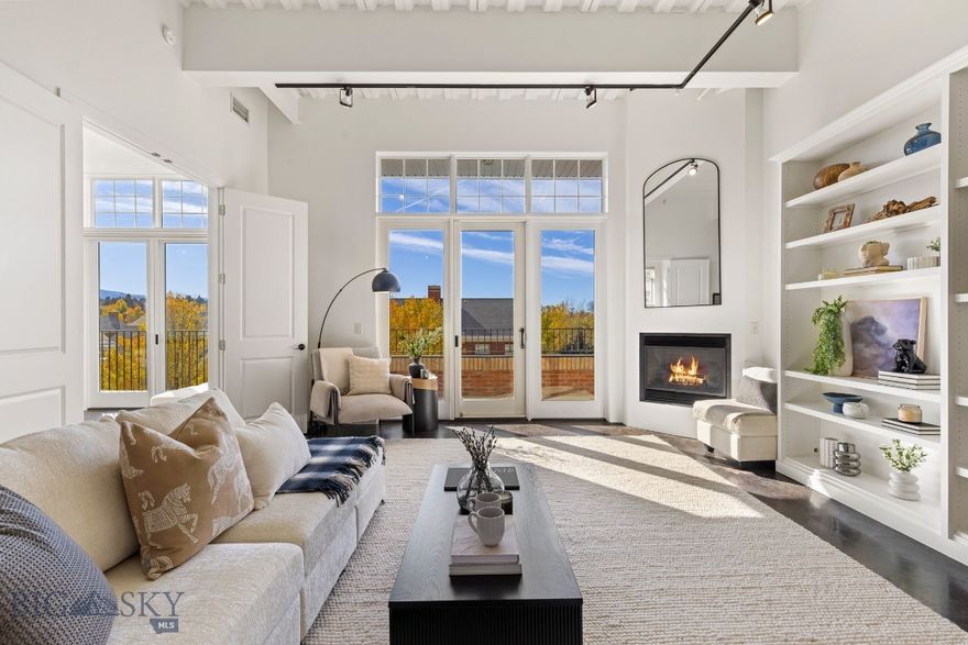 Experience elevated downtown living in this beautifully appointed corner unit at The Village Downtown. Thoughtfully designed and impeccably maintained, this two-bedroom, two-bath condo features southwest views and an abundance of natural light. The open floor plan and 12 foot ceilings make the space feel larger than its already generous 1,414 square feet. Every element feels intentional, from the custom entryway to the bespoke reclaimed-wood island - an artful blend of craftsmanship and character. The adjacent living area is anchored by custom built-ins and a gas fireplace, offering both warmth and sophistication. The primary bedroom with an ensuite bath features dual vanities, dual closets, and a walk-in shower with soaking tub. It's an ideal spot to unwind after a day in the mountains or an evening downtown. Radiant floor heating and air conditioning ensures year-round comfort. Custom shelving in all the closets adds modern function to every room. Step out to your private patio to enjoy Bozeman’s vibrant sunsets or unwind with friends on a summer evening. With a designated underground parking space, secure storage, and effortless access to Downtown’s shops, dining, and trails, this condo offers a lifestyle that’s as convenient as it is luxurious. It’s more than a place to live, it’s a modern retreat designed for those who value simplicity, comfort, and refined living in the heart of Downtown Bozeman.