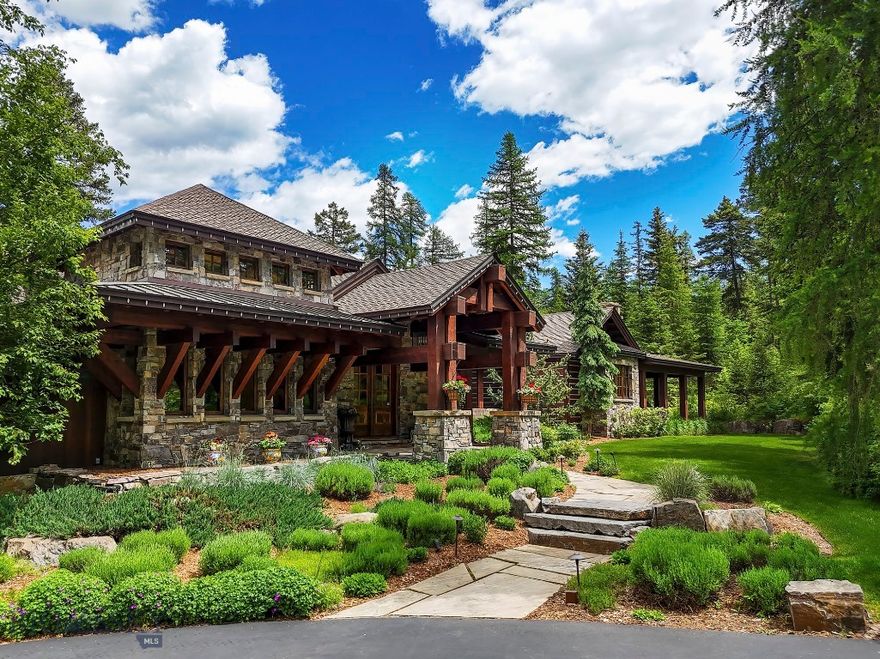 Located within the gated privacy of Whitefish Hills, 1263 Spencer Ridge Road takes full advantage of one of the best 20 acre lots in the development with views of the Whitefish & Swan Mountain Ranges and stunning views into Glacier National Park and Mt. Jackson. These views are celebrated from virtually every room in this timeless Montana residence of stone, timber and wood handcrafted around a thoughtful and efficient home design to a level of detail rarely experienced. This meticulously maintained residence is blended into the hillside and lives seamlessly with the outdoors from various decks and stone patios surrounded by mature landscaping, terraced elevation changes and a water feature whispering falling water to the private primary bedroom wing. A series of connected trails makes it easy to venture farther from the home to enjoy the remaining 20 acres of thinned and professionally maintained forest and the serene shore of a shared lily pond below the home. 
Upon entry from stone steps set under massive timber trusses the home welcomes you with a feeling of warmth and comfort exuded from colors, textures and materials blended in a style of refined Montana rustic. Plaster walls, stained alder trim and doors, sturdy bronze hardware, wood burning stone fireplaces and distressed hardwood floors set the tone while being complimented by top of the line plumbing and light fixtures, appliances, cabinetry and stone countertops. The additional comforts of radiant heat flooring, central air conditioning, Russound sound system and Lutron controlled lighting system round out the amenities of a truly custom home experience. From the main entry foyer the home flows into a comfortable open concert of great room, dining area, kitchen and sit up bar all accessing outdoor decks. An incredibly private main floor primary bedroom wing is connected by an impressive glass and stone gallery while the open stairwell makes the transition to the lower level with three additional ensuite bedrooms, family and game room, bar, gym, office, theatre and wine room. Connecting easily from the kitchen, the stone floor mudroom makes the transition to the large three car garage and a full guest apartment above while the detached shop located a few steps from the main home adds additional car and toy storage and guest quarters above. Complimented by the amenities of Whitefish Hills and shared access to Blanchard Lake this home and location are priced at a true value for your buyers.