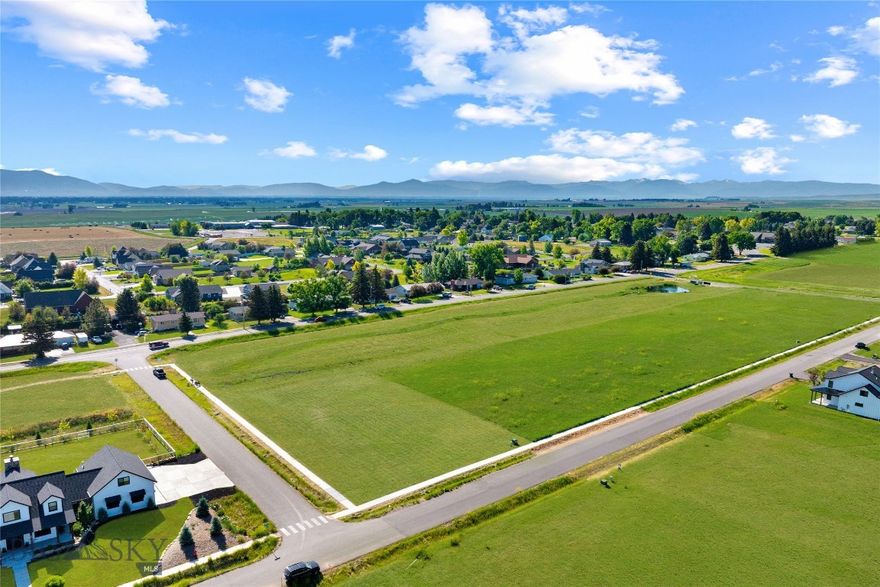 This coveted ½-acre corner lot sits in a walkable luxury development that allows ADUs and backs to open, HOA-maintained park space. The lot is fully equipped for construction with natural gas, power, fiber optic (1 GB download speed), and a community sewer system already in place. Buyer is responsible only for a private well and final plan approval with the builder. Nearby well logs show a strong 30 GPM yield at 241 feet.

Included are thoughtfully designed modern farmhouse plans featuring 4 bedrooms, 4 bathrooms, and just under 4,000 square feet. The home offers both formal and relaxed living areas, a main-level primary suite with ensuite bath and walk-in closet, an open-concept kitchen, dining, and living room, a walk-in butler’s pantry, mudroom/laundry, dedicated office, and a three-car garage. Step outside to an 18’ x 14’ covered patio with a fireplace—perfect for Montana’s indoor-outdoor lifestyle.

A large detached garage/shop is also part of the plans—ideal for trucks, trailers, tools, and hobbies. Above it sits a private-entry ADU with a bedroom, bath, kitchenette, and open-concept living—perfect for guests, multi-gen living, or office use. Driveway access to both the attached and detached garages comes from Goffman Lane on the north side of the property, while the front of the home faces Cushing Lane to the west. This layout provides privacy with the garage and shop shielding views of neighboring properties, while the backyard opens to southern exposure and stunning views of the snow-capped Spanish Peaks.

Enjoy big skies, sweeping mountain views, and the soft soundtrack of crickets and wind in the grass from the surrounding farmlands. Life here moves at a peaceful, steady pace—tucked between Amsterdam and Churchill, where community and quiet still matter. You’ll be near well-regarded K–12 schools offering AP classes and sports across all grades, and just minutes to the Bozeman Airport, shopping, dining, gyms, and more.

Located just 16 minutes to the airport, 15 minutes to Cottonwood Hills Golf Course, and 25 minutes to downtown Bozeman. Outdoor recreation abounds—45 minutes to Bridger Bowl, 1 hr 10 min to Big Sky, and 50 minutes to Hyalite Reservoir. Hit the College ‘M’ trail (30 min), ride ATVs at Pipestone (50 min), or fish the nearby rivers.

However you choose to enjoy Montana, this location puts it all within reach.