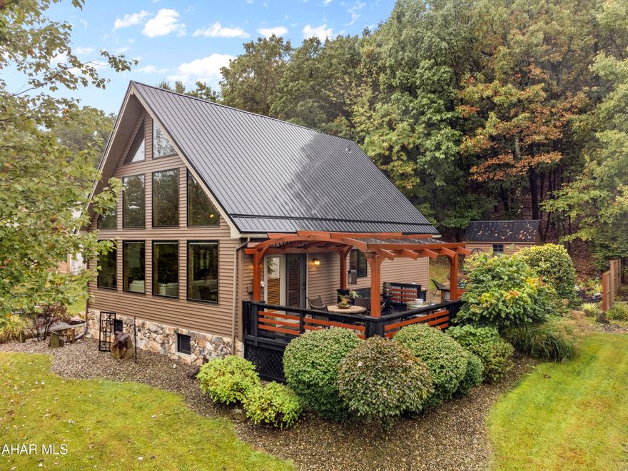This stunning 3-bedroom home is nestled in the serene and picturesque Beverly Hills neighborhood of Altoona, PA! This architectural gem combines rustic charm with modern luxury, perfect for those looking for a unique and cozy retreat. As you approach the home, you are greeted by the signature steeply sloped roofline that maximizes space and allows for breathtaking views. The exterior features rich, natural woodgrain vinyl siding that blends seamlessly into the landscape, giving you the feeling of living in a private woodland landscape. Step inside the main floor and you will be welcomed by a spacious, open concept living area with soaring ceilings that fill the space with natural light. The large floor-to-ceiling windows bring the beauty of the outdoors inside, offering panoramic views of lush greenery in the summer and beautiful fall colors in the fall. The living room has a modern fireplace that creates a warm and inviting atmosphere that is perfect for relaxing on cool Pennsylvania evenings. The gourmet kitchen is outfitted with sleek, modern appliances, custom cabinetry, and a peninsula that is ideal for entertaining guests. The main floor also offers 2 bedrooms and a full bathroom with modern fixtures. Upstairs, you will find the primary bedroom with ensuite bath with modern finishes and a private deck overlooking the private backyard. The lower level of this home features a family room, a wet bar with plenty of storage for your party supplies and a 1/2 bath and an infrared spa meditation rom. Outside, the deck provides the perfect spot for enjoying morning coffee or evening sunsets while surrounded by nature. This A-frame home offers the perfect balance of secluded tranquility and accessibility, being just a short drive from downtown Altoona's amenities, shops and restaurants. This home is the perfect blend of rustic charm and modern living in a setting that feels like a permanent vacation.