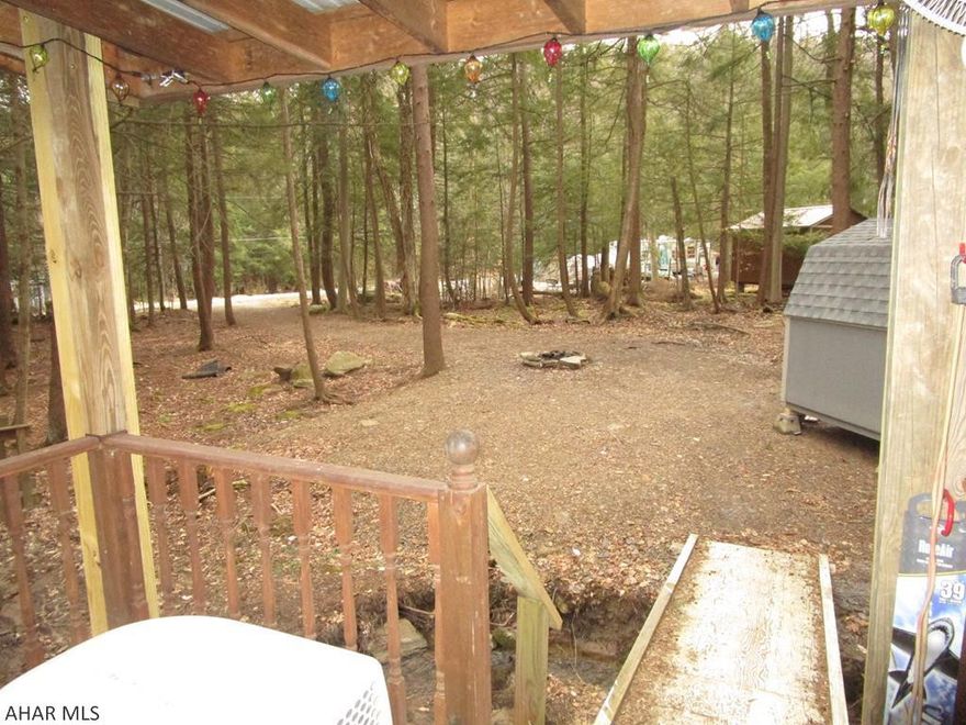 This campsite is ready for placing your camper.  The sellers have a 39' camper so you can be sure there is room for any unit.  A creek runs through the property adding to the perfect setting for being in the woods.  The utilities (water, sewer, electricity) are on the narrow end of the campsite so that is where your camper would need to be situated.  There is a covered deck for outside living regardless of precipitation.  A bridge fords the stream to connect you to the wooded area where the campfire area and shed are located.  An access road allows you to drive into the rear of the lot.  The access road is common ground but can be used by those whose lots are adjacent to it.  No camper?  The sellers will consider selling the camper as well.