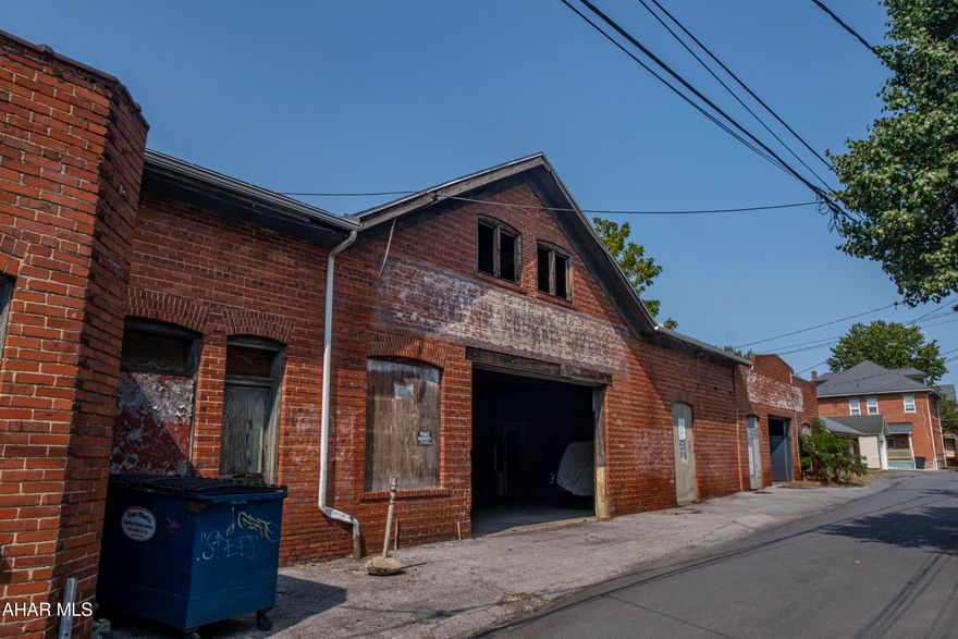 Income-producing garage and warehouse property in the heart of Hollidaysburg's Historic District. Accessed via Cherry Alley, this substantial 8,125 sq ft brick structure offers immediate revenue generation with long-term investment potential.

Building Details:

The 1.5-story property comprises three connected sections built circa 1850 with solid brick construction:

Garage space: 4,520 sq ft

Warehouse: 3,605 sq ft


The brick exterior features arched windows and doorways and decorative brickwork characteristic of mid-century commercial construction. Exposed wood beam and joist ceiling structure creates impressive height throughout, with a two-story section adding vertical storage or workspace potential.

Courtyard & Outdoor Space:

A private 750 sq ft courtyard provides additional functional outdoor space for loading, storage, or future improvements. 

Current Use & Income:

Currently generating rental income from leased parking spaces with multiple open garage bays and covered warehouse space. The flexible layout includes drive-through access, concrete floors, and numbered parking stalls--ideal for continued parking operations or reimagined use.

Location & Access:

Situated on a 0.25-acre lot (122' x 88') accessed via Cherry Alley, just off Walnut Street in Hollidaysburg Borough's historic downtown. The property is zoned R-2 (General Residential) and assessed as CC-Commercial Combination, located within the Historic Resources Overlay District. Level terrain with paved alley access, public water, sewer, and gas all available on-site.

Versatile Potential:

The substantial square footage, exposed beam construction, and central location create opportunities for various uses:

Continue income-generating parking operation

Workshop or maker space

Vehicle/equipment storage

Warehouse/distribution

Mixed-use conversion (subject to municipal approvals)

Property is within the Historic Resources Overlay District; certain alterations may require HARB review.

A rare opportunity to acquire a large-scale commercial structure with established income in Hollidaysburg's downtown core.

Additional Information:
The historic Victorian residence and cottage at 418 N Montgomery Street is also available for purchase (see MLS# 78432). Both properties can be acquired together for expanded possibilities, or this garage may be purchased independently. Each property offers distinct value and functionality on its own.