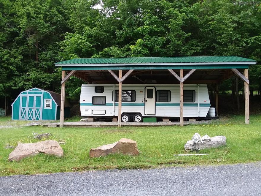 Two spacious flat wooded lots just at the bottom of the hill from the swimming pool / clubhouse. Large shed.  Newer pavilion covers the camper which has two sleeping areas.  Camper is older but in good shape.  Property is located on a dead end road.