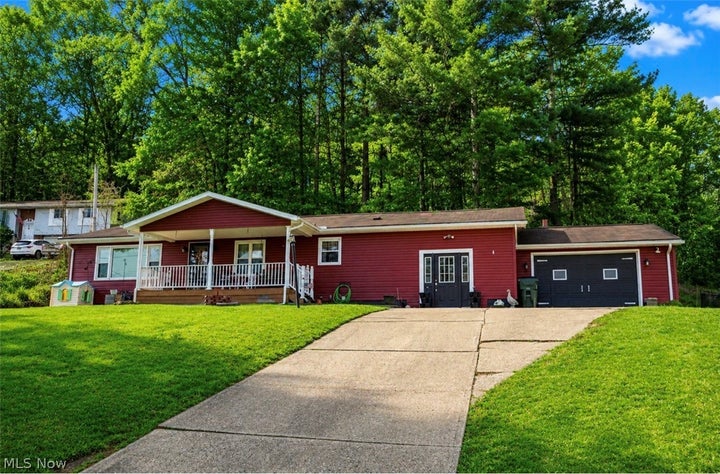 Ranch-style house with driveway, a trampoline, a garage, an outbuilding, and covered porch