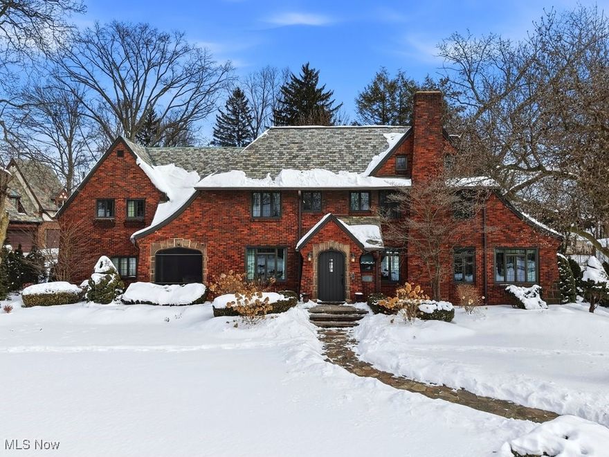 A distinguished 1928 all-brick Tudor, gracefully set above the street with exceptional curb appeal & timeless storybook presence. Sandstone retaining walls, manicured landscaping, a stone walkway & steps create a striking approach to the original wood front door, setting the tone for the craftsmanship found throughout. Inside, the entry foyer feat. HW floors & opens to a spacious 15x23 family room w HW flooring & a beautiful fireplace. French doors lead to a sunroom surrounded by windows, offering a warm, light-filled retreat. The dining room feat. hardwood floors & French doors opening to a timeless screened porch w slate flooring. A classic butler’s pantry connects the dining room to the charming breakfast nook w a distinctive hexagonal window, located just off the updated kitchen. The kitchen (reno in '22) offers white cabinetry, granite countertops, hardwood floors & a suite of stainless steel appliances (Fisher & Paykel range & fridge). Additional main-level highlights incl. an adorable half BA tucked under the staircase & french door leading to the backyard. Outdoors, a raised stone patio, driveway w brick inlay, koi pond, firepit & charming ivy-covered potting shed create a private garden retreat. Upstairs, the primary suite is truly showstopping- feat. dramatic 2-story vaulted ceiling, hardwood floors & a striking gas fireplace framed by high-end millwork. Symmetrical windows flood the space w natural light, while built-in chestnut bookcases add warmth & depth. The suite feat. 2 closets & private en-suite BA. 4 additional BRs & 2 full baths (incl. an ensuite w clawfoot tub), abundant closets, original built-in linen cabinet & a light-filled stair landing reflect the home’s enduring craftsmanship. The 3rd floor provides generous 31x16 bonus room w vaulted ceilings. 1 furnace '24, 25 windows replaced '21. With over 3,200 sqft of living space, this grand yet cozy Tudor is a rare piece of Akron history—rich in character, thoughtfully updated, and truly special.