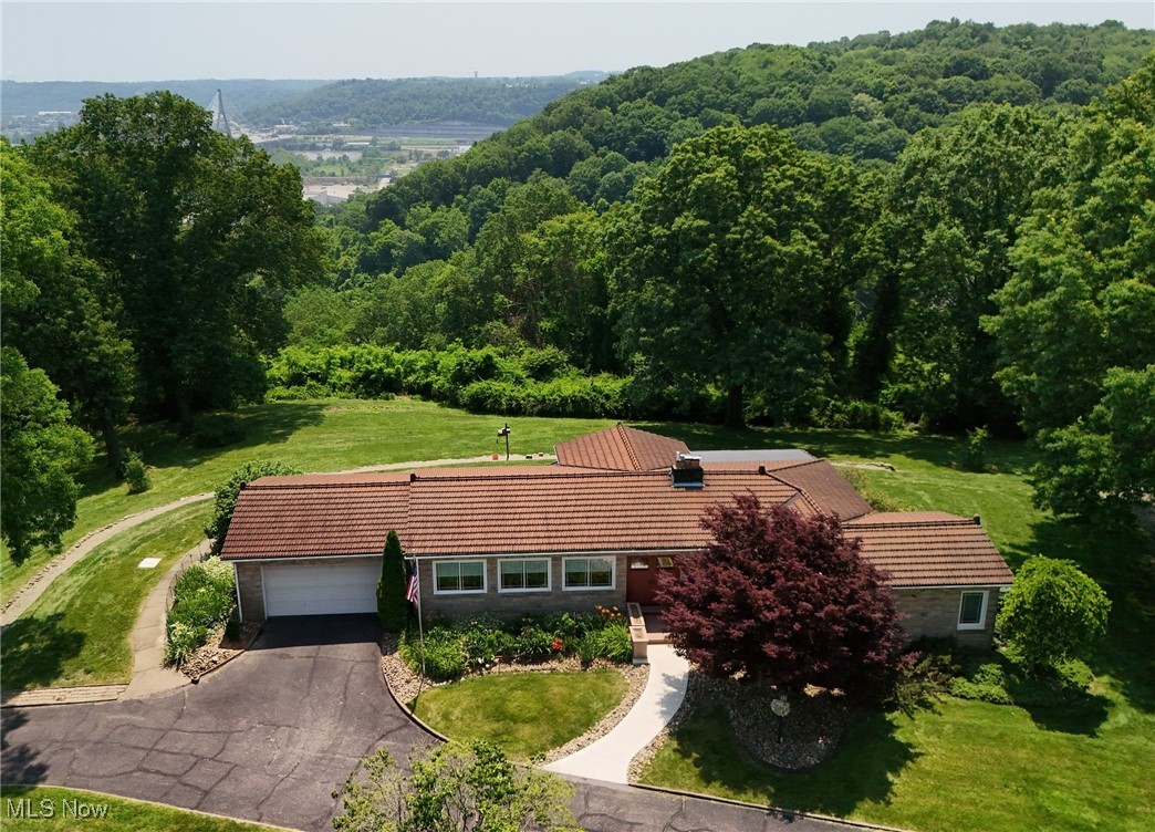 Don't miss this rare opportunity to own a truly special property with breathtaking views of the Ohio River and the Veterans Memorial Bridge. From the moment you arrive, you'll be greeted by a gracious governor's driveway surrounded by lush landscaping and mature trees offering a grand first impression. Step through elegant double doors designed to impress. At the back, massive sliding glass doors frame panoramic views of the river, bringing the outdoors in. The tv room and breakfast nook feature unique cork flooring, while the updated kitchen shines with stainless steel appliances. The dining room includes built-in cabinetry and beautiful hardwood floors. The spacious living room boast high ceilings, a cozy fireplace, hardwood flooring, and two sets of sliding glass doors leading to the deck and back yard-ideal for relaxing or entertaining. What a great place to watch the holiday fireworks display! The main level offers 3 bedrooms and 2 full bathrooms, all thoughtfully laid out for comfort and privacy. Downstairs, the walk-out basement is expansive, with a massive laundry room, abundant storage, a rec room and a workshop. It offers two separate entrances-one from the oversized garage and another from the main hallway-it's functional as it is spacious. The home is topped with elegant tera cotta roof tiles, and the 3.4-acre property has been recognized as a WV Wild Yard by the state of WV-a testament to its natural beauty and ecological value. As an added bonus, this property included a fully furnished 1-bedroom 1 bath guest cottage, with its own basement and 1 car garage-perfect for hosting visitors or generating extra income. This property is truly one-of-a-kind-spacious, serene, and full of character with unbeatable views. Schedule your private showing today!