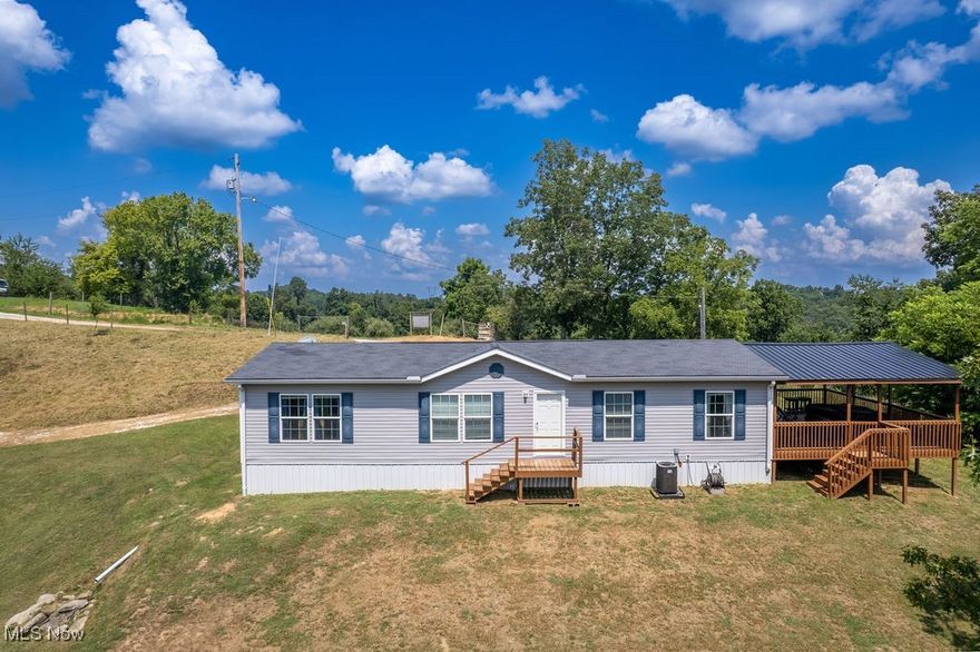 Enjoy the simplicity of one-floor living with this beautifully crafted home on nearly an acre. A striking covered deck with panoramic views sets the tone for the peaceful country setting, where wildlife and rolling hills create a scenic backdrop.

Inside, natural light highlights custom touches throughout, including full drywall walls, 2x6 construction, and thoughtfully designed built-ins. The open layout flows from the dining area with a coffered ceiling to a bright kitchen with an island, abundant cabinetry, and a deep farmhouse sink, all framed by a graceful arched entry to the living room.

As you enter, you’re greeted by a built-in cubby area with a cozy bench, overhead storage, and compartments perfect for keeping shoes, coats, and everyday items neatly organized. Beyond this space, the laundry area offers an efficient L-shaped design with upper and lower cabinetry for ample storage and a sink positioned beneath a window, adding both function and natural light. The laundry area also connects directly to the mechanics room.

Two secondary bedrooms are tucked off the hallway, each featuring large closets. The nearby full bathroom includes a traditional tub and shower combination, serving these bedrooms and guests with ease. The private primary suite offers a spacious retreat with a generous walk-in closet and a beautifully finished bathroom featuring a dual vanity, extra cabinetry, and a large walk-in shower.

Beyond the walls of this home lies a space meant to be savored. The covered deck is ideal for hosting friends, watching storms roll across the hills, or quietly observing deer and other wildlife. A whole house generator and storage building add both practicality and peace of mind, completing this blend of comfort and country