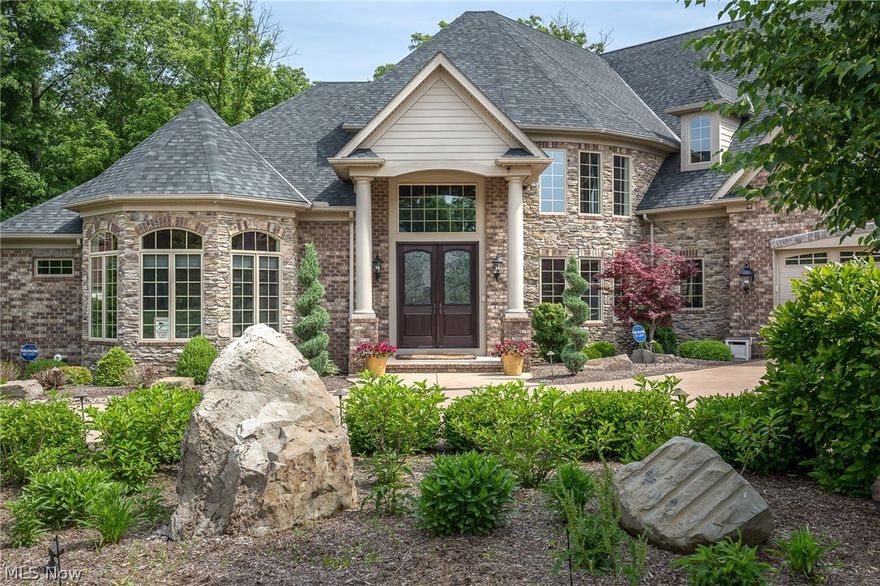 Absolutely gorgeous & remarkably appointed custom ALL brick & stone home in impeccable condition, on 2.0 stunning & private park-like acres, offers spectacular views of the pristine landscaping, waterfall feature, low lying stream, woods, stamped concrete patio & walkways, firepit, foot bridge, Trexx Deck, & heated outdoor kitchen with new gas grill, bench seat, fireplace, vaulted wood ceiling, pizza oven, sink, removable windows & more! This home is best suited for those who love to entertain inside and out. The home has high ceilings, very open floor plan, exquisite luxury finishes & architectural details, tons of closet & storage space, an elevator that services ALL 3 levels, & upper & lower heated garages that can house up to 10 cars plus a car lift & workshop. There is a large 2 story foyer with coffered ceiling, a library with built-ins, great room with a stunning coffered ceiling, an open concept gourmet eat-in kitchen with adjoining dining room & a hearth room with fireplace &