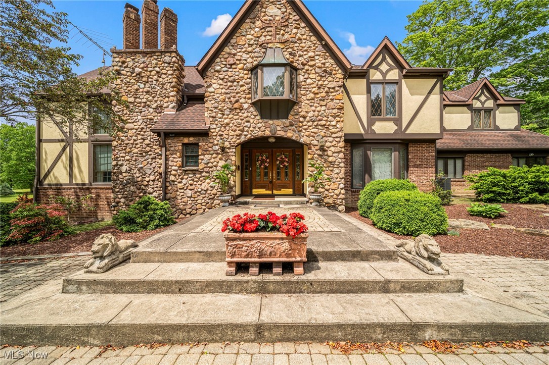 This architectural gem is a masterfully crafted English Tudor estate, meticulously built over a 30-year period. The home is a showcase of exquisite woodwork, with cherry wood in the living room and wooden beams in the back family room sourced directly from the property. The two-story living room features a stunning wall of windows and a view of the library on the second level. The expansive kitchen is a chef’s dream, featuring two refrigerators, double stove top with double ovens, and two dishwashers. A large office is conveniently located on the first floor. There are four spacious bedrooms each offering their own bathroom. The grand master suite is a retreat in itself, with french doors opening to the rooftop of the original home. The suite includes a lavish walk-in closet that doubles as a dressing room, complete with built-in dressers and organizers. The finished lower level is an entertainment haven, featuring a full bar, pool table, air hockey, and skee ball. The estate is set on 61.25 serene acres, offering a peaceful country setting with a pond, a large outbuilding ideal for a workshop or car collection, and a second smaller outbuilding. A circular driveway graces the front, while a second drive leads to the back entrance and the attached two-car garage.
