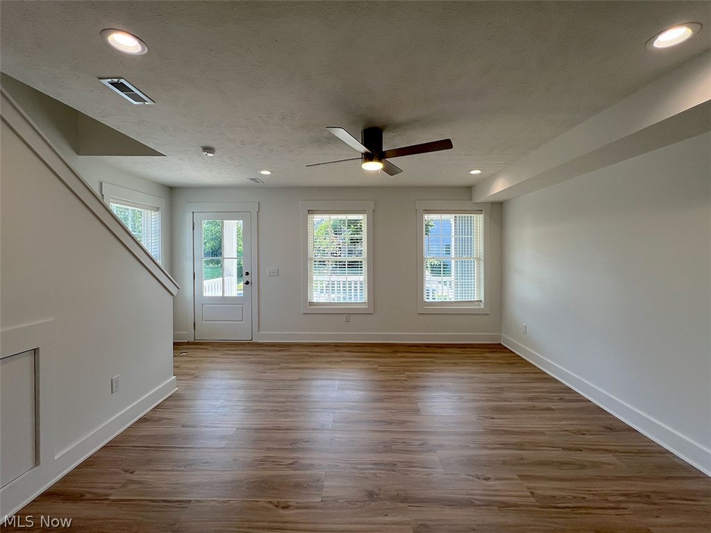 Open concept livinng/dining area with bank of front windows allowing vast natural light, wood-type flooring, a chandelier, ceiling fan, and recessed lighting