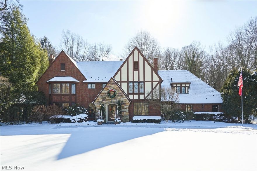 In the heart of Fairlawn Heights, this 1929 Tudor offers the rare combination of architectural pedigree and everyday livability. Set on nearly one acre, the property unfolds with a circular drive, level grounds, & a sense of quiet presence that defines West Akron’s most established addresses. A stone entry leads to a charming vestibule & gracious foyer, where oversized original leaded-glass windows flood the interiors with natural light. Rich hardwood floors, painted moldings, and stained trim create a refined balance of warmth and contrast. The scale is timeless; the detailing unmistakable. The Living Room is anchored by a carved limestone mantel and framed by leaded doors opening to the Sunroom—an all-season retreat with separate heat and serene views of the front and rear grounds. Just beyond, the paneled Family Room offers built-ins, a bay window, and a second fireplace. The Dining Room is generously proportioned and includes a silver closet for effortless entertaining. The updated Kitchen features granite counters, pantry storage, newer appliances, w/access to the stone patio. Its adjoining breakfast room is as charming as it is practical. A rear hall w/storage and vintage powder room adds function without sacrificing character. Upstairs, 5 bedrooms and 4 full baths provide remarkable flexibility. The primary suite includes two closets, a dressing room, and two attached baths, one with separate tub & shower, both with heated floors. A discreet second-floor laundry enhances daily ease. The lower-level Rec Room, with a brick fireplace and new flooring, offers additional living space, along with abundant storage and the original laundry. A 3-car garage completes the home. Professionally maintained slate roof, newer HVAC, and thoughtful updates throughout reflect exceptional stewardship. A stone patio wraps the rear of the home, overlooking private, park-like grounds with open lawn and wooded edges. A Tudor of substance, scale, and soul—ready for its next chapter.