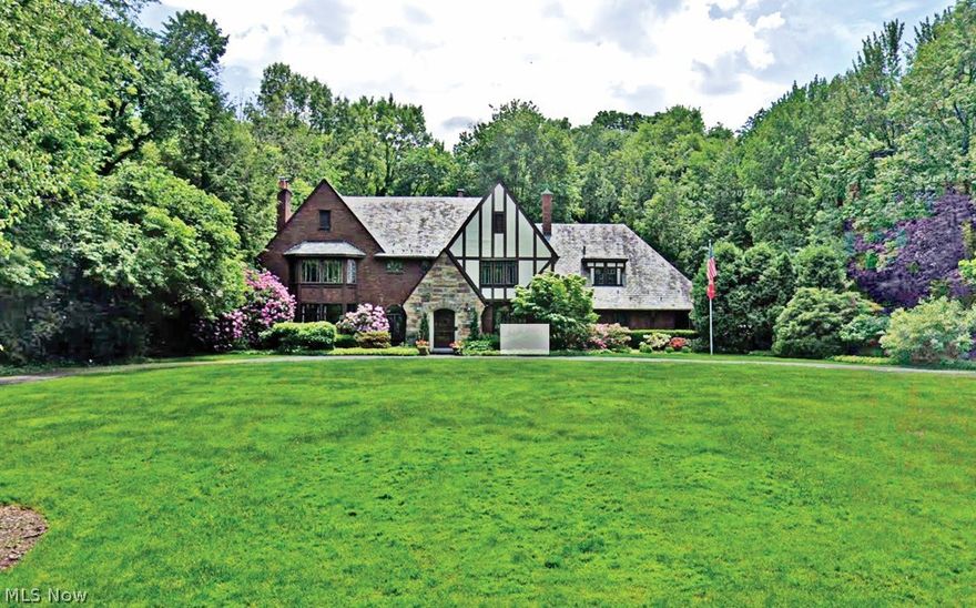 In the heart of Fairlawn Heights, this 1929 Tudor offers the rare combination of architectural pedigree and everyday livability. Set on nearly one acre, the property unfolds with a circular drive, level grounds, & a sense of quiet presence that defines West Akron’s most established addresses. A stone entry leads to a charming vestibule & gracious foyer, where oversized original leaded-glass windows flood the interiors with natural light. Rich hardwood floors, painted moldings, and stained trim create a refined balance of warmth and contrast. The scale is timeless; the detailing unmistakable. The Living Room is anchored by a carved limestone mantel and framed by leaded doors opening to the Sunroom—an all-season retreat with separate heat and serene views of the front and rear grounds. Just beyond, the paneled Family Room offers built-ins, a bay window, and a second fireplace. The Dining Room is generously proportioned and includes a silver closet for effortless entertaining. The updated Kitchen features granite counters, pantry storage, newer appliances, w/access to the stone patio. Its adjoining breakfast room is as charming as it is practical. A rear hall w/storage and vintage powder room adds function without sacrificing character. Upstairs, 5 bedrooms and 4 full baths provide remarkable flexibility. The primary suite includes two closets, a dressing room, and two attached baths, one with separate tub & shower, both with heated floors. A discreet second-floor laundry enhances daily ease. The lower-level Rec Room, with a brick fireplace and new flooring, offers additional living space, along with abundant storage and the original laundry. A 3-car garage completes the home. Professionally maintained slate roof, newer HVAC, and thoughtful updates throughout reflect exceptional stewardship. A stone patio wraps the rear of the home, overlooking private, park-like grounds with open lawn and wooded edges. A Tudor of substance, scale, and soul—ready for its next chapter.