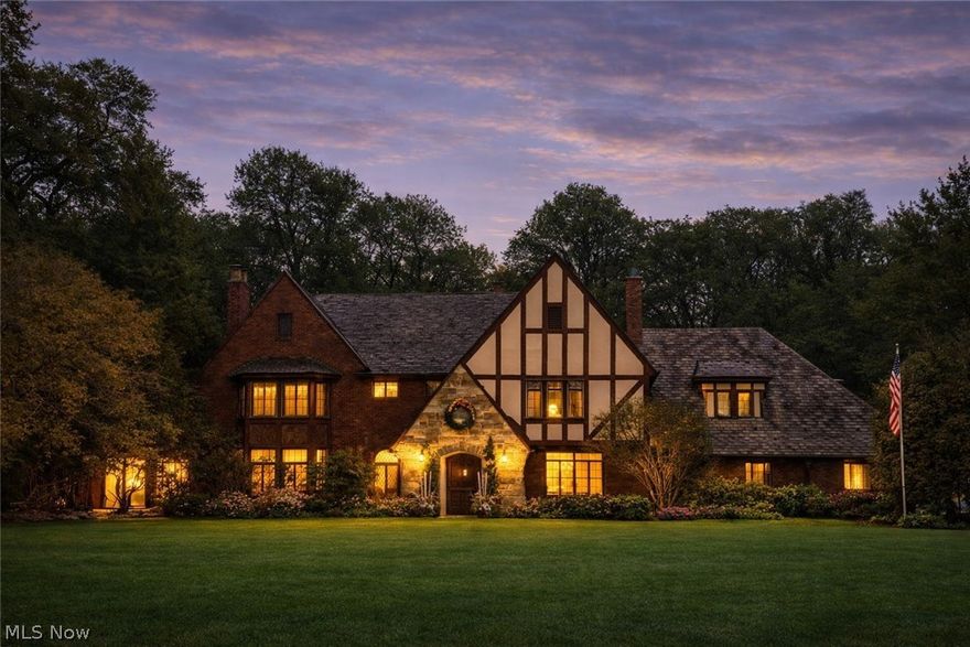 In the heart of Fairlawn Heights, this 1929 Tudor offers the rare combination of architectural pedigree and everyday livability. Set on nearly one acre, the property unfolds with a circular drive, level grounds, & a sense of quiet presence that defines West Akron’s most established addresses. A stone entry leads to a charming vestibule & gracious foyer, where oversized original leaded-glass windows flood the interiors with natural light. Rich hardwood floors, painted moldings, and stained trim create a refined balance of warmth and contrast. The scale is timeless; the detailing unmistakable. The Living Room is anchored by a carved limestone mantel and framed by leaded doors opening to the Sunroom—an all-season retreat with separate heat and serene views of the front and rear grounds. Just beyond, the paneled Family Room offers built-ins, a bay window, and a second fireplace. The Dining Room is generously proportioned and includes a silver closet for effortless entertaining. The updated Kitchen features granite counters, pantry storage, newer appliances, w/access to the stone patio. Its adjoining breakfast room is as charming as it is practical. A rear hall w/storage and vintage powder room adds function without sacrificing character. Upstairs, 5 bedrooms and 4 full baths provide remarkable flexibility. The primary suite includes two closets, a dressing room, and two attached baths, one with separate tub & shower, both with heated floors. A discreet second-floor laundry enhances daily ease. The lower-level Rec Room, with a brick fireplace and new flooring, offers additional living space, along with abundant storage and the original laundry. A 3-car garage completes the home. Professionally maintained slate roof, newer HVAC, and thoughtful updates throughout reflect exceptional stewardship. A stone patio wraps the rear of the home, overlooking private, park-like grounds with open lawn and wooded edges. A Tudor of substance, scale, and soul—ready for its next chapter.