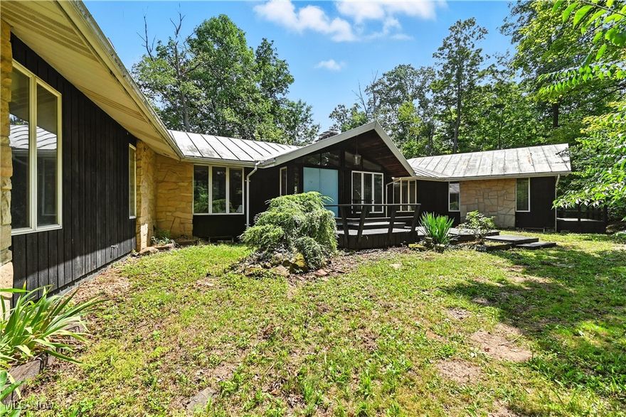 This sprawling 4,775 sq ft, 8-bedroom, 4.5-bath home is full of character, history, and potential. Thoughtfully constructed with architectural pieces salvaged from historic homes in the area, every detail tells a story. At the heart of the home, a stunning spiral staircase leading down to the finished basement- crowned by a full stained-glass wall, which is an unforgettable focal point. The home features unique touches throughout, including an original intercom system, built-in glass display shelving with lighting, and four fireplaces upstairs. The lowered family room boasts vaulted ceilings with exposed decorative beams and opens to a walk-out deck that spans the entire length of the home, perfect for entertaining or relaxing above the treetops. Downstairs, the basement is ready for guests or extended living with two additional bedrooms, a second kitchen, fireplace, wet bar, and even a darkroom. This property is a rare opportunity for someone with vision.