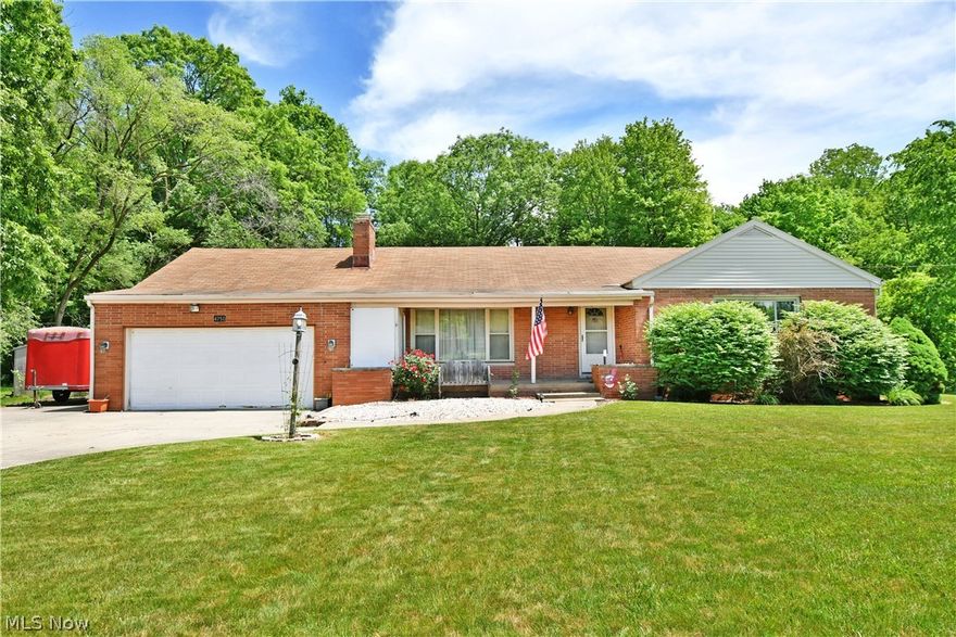 Hurry in, this three-bedroom Austintown ranch won’t be around for long! Showcasing an endearing brick faced exterior, this potential packed residence enjoys a high demand location and a fantastic property with a scenic wooded backdrop.  The oversized cement driveway opens to a wide apron, offering easy additional storage or parking next to the attached two car garage. An additional gravel turnaround waits under the shady trees. Inside, a tiled foyer leads through sculpted entryways as it first presents the expansive living room. Here, hardwood flooring continues to the stone lined accent wall with its inset fireplace. Hidden shelf overhead lighting joins the large picture window to illuminate the room. Around the corner, a formal dining room yields its own tall windows for great backyard views. A galley styled kitchen spans the adjoining hall, trimmed in emerald-colored countertops and paired with piano black appliances. Casual dining is located near garage access. Opposite the foyer, three bedrooms branch from the main hallway. Included is the oversized master with its multiple closets. The floor is completed by a deep-set bath brimming with colorful tiles. A full basement is located below to include laundry and workshop spaces.