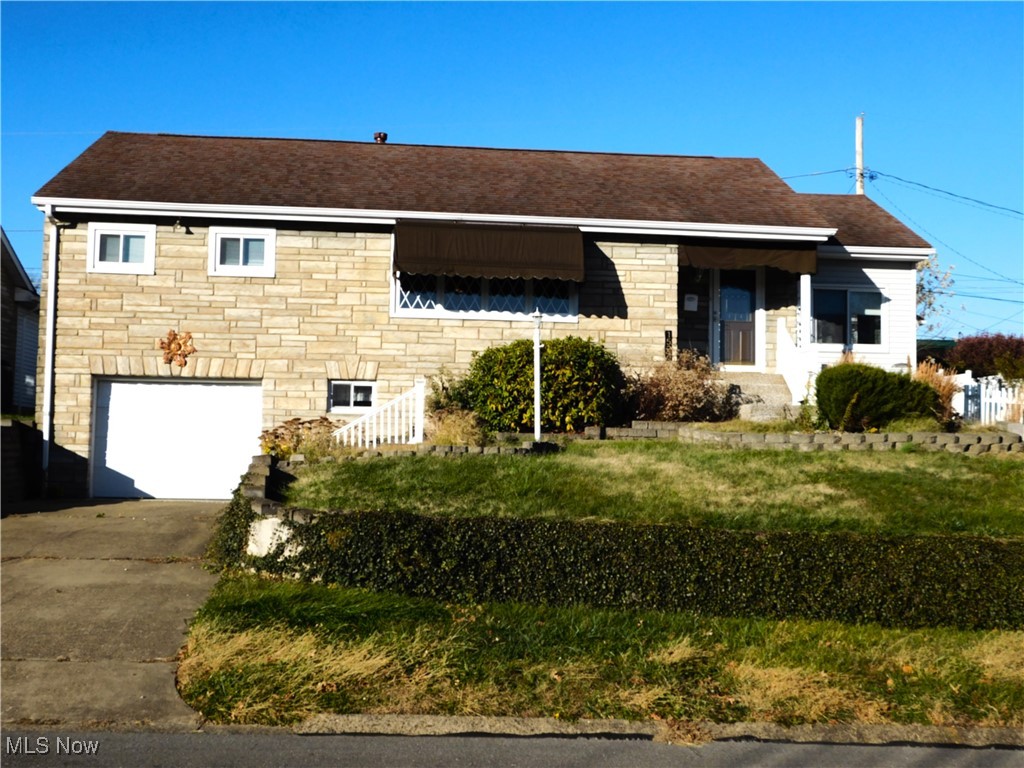 View of front of home with stone siding, a garage, concrete driveway, a front lawn, and a shingled roof
